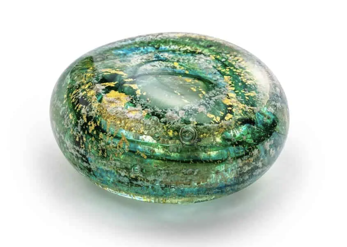 A green and gold glass memorial keep sake with cremated ashes, 4cm wide 1.5cm deep