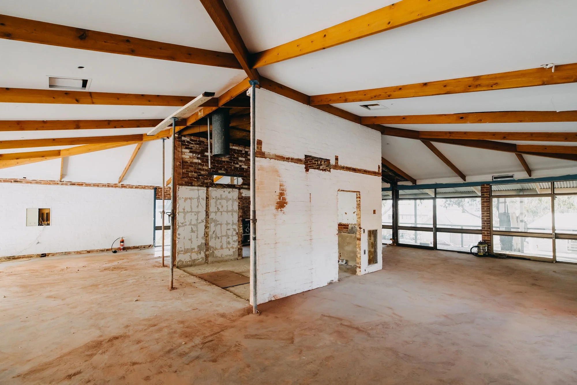 Interior of a building under construction with exposed wooden beams on the ceiling and unfinished walls and flooring.