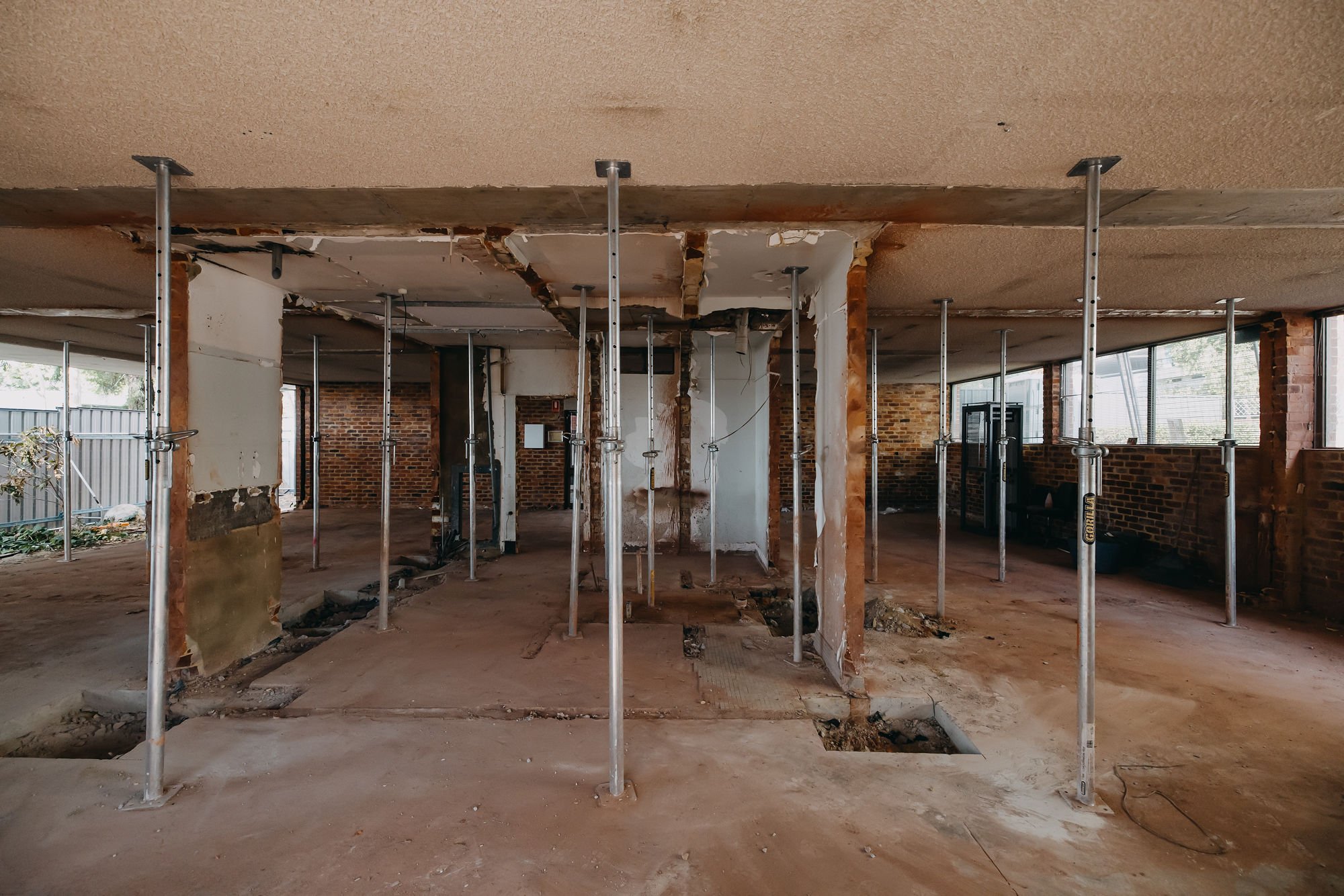 Interior of a building under renovation with exposed brick walls, support beams, and construction scaffolding.