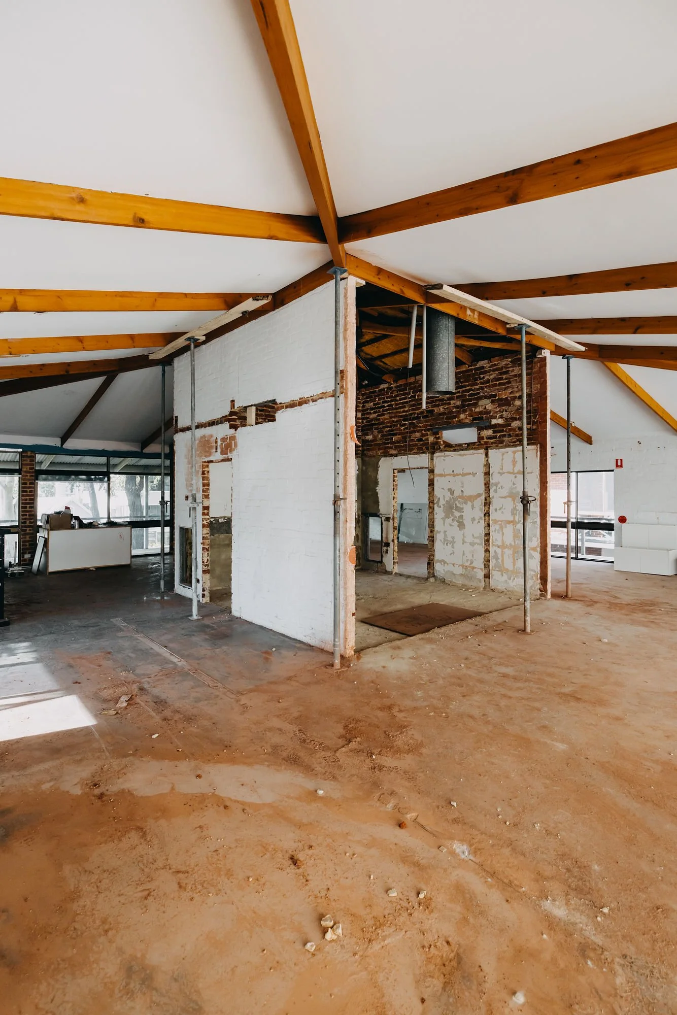 Interior of a building under renovation with exposed brick walls, construction supports, and a dirt floor.