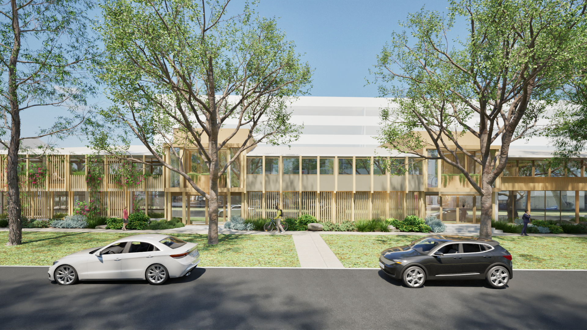 A modern building with large windows and wooden accents, surrounded by trees and landscaping, with two cars parked on the street in front.