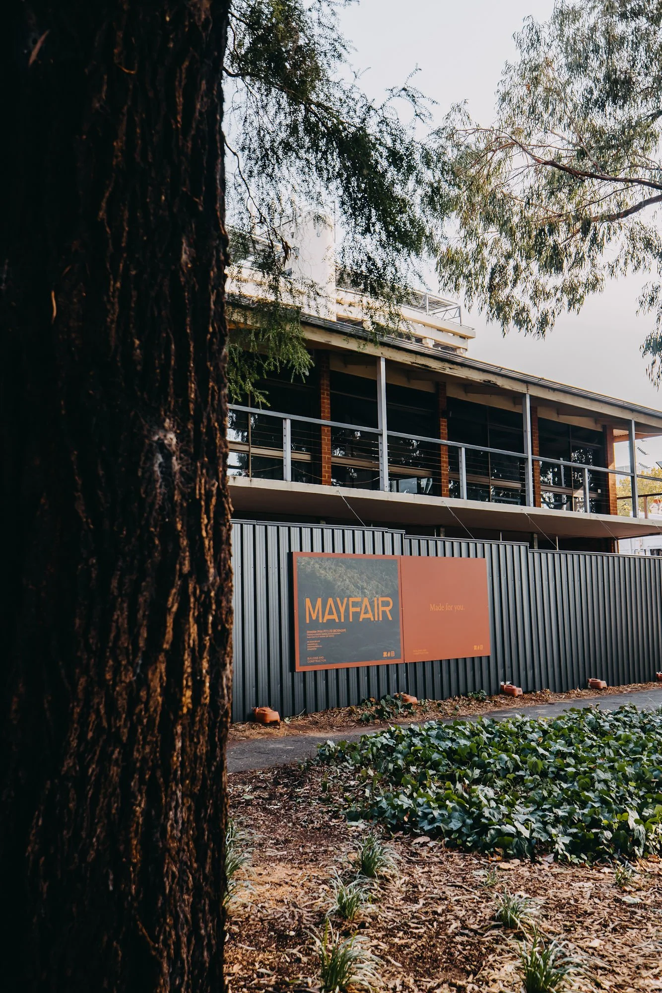 A building with a black fence in front, a large sign that reads 'MAYFAIR,' and trees surrounding the area.