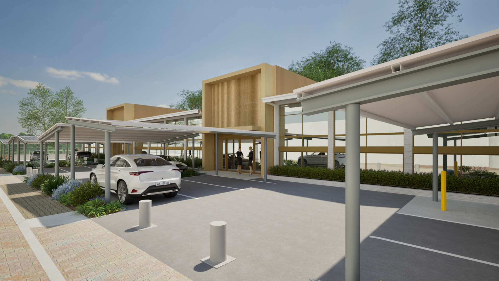 Modern building with parking lot, covered parking spots, and greenery, with two people standing near the entrance.