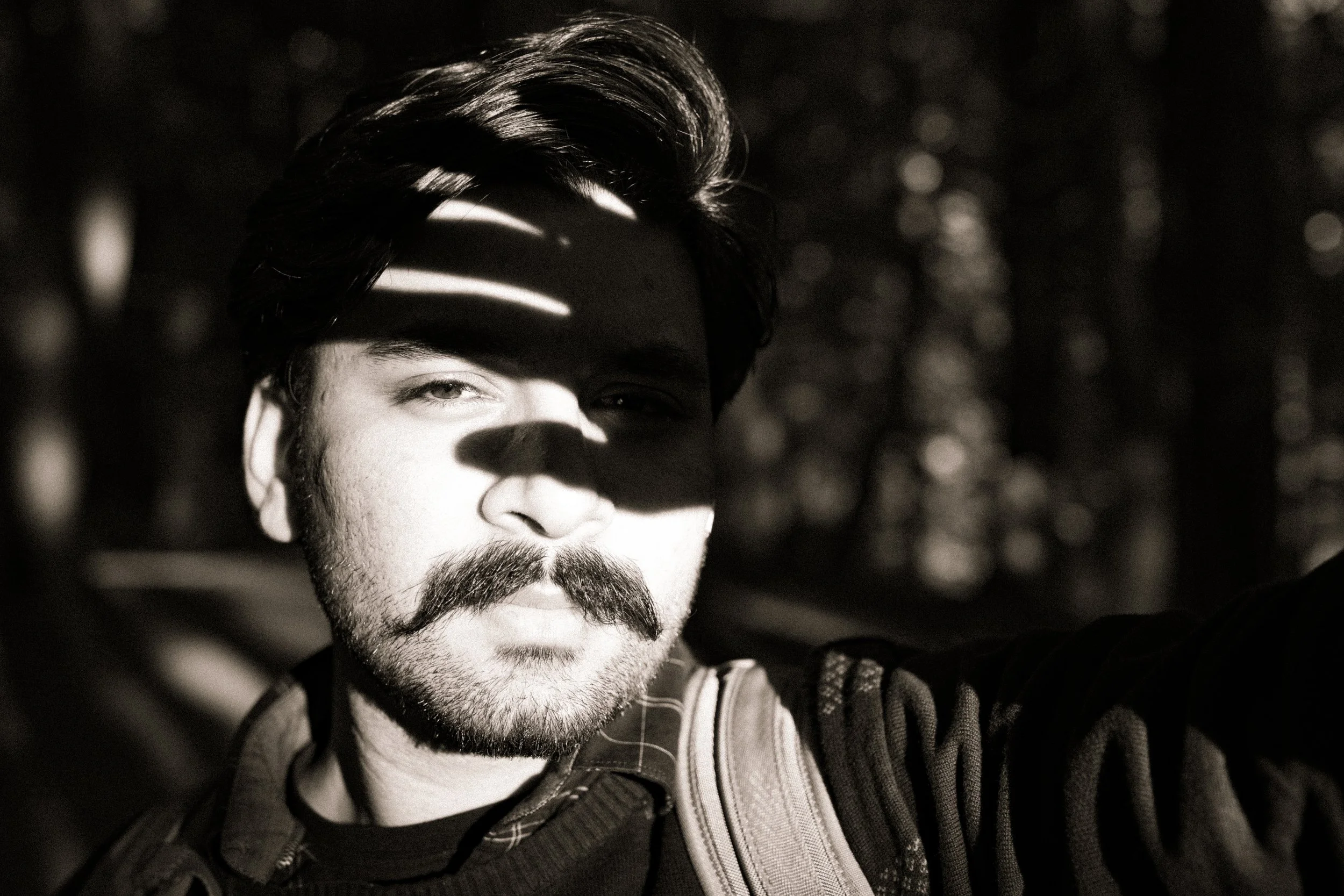 Man with mustache in shadowy lighting holding hand to block sunlight.