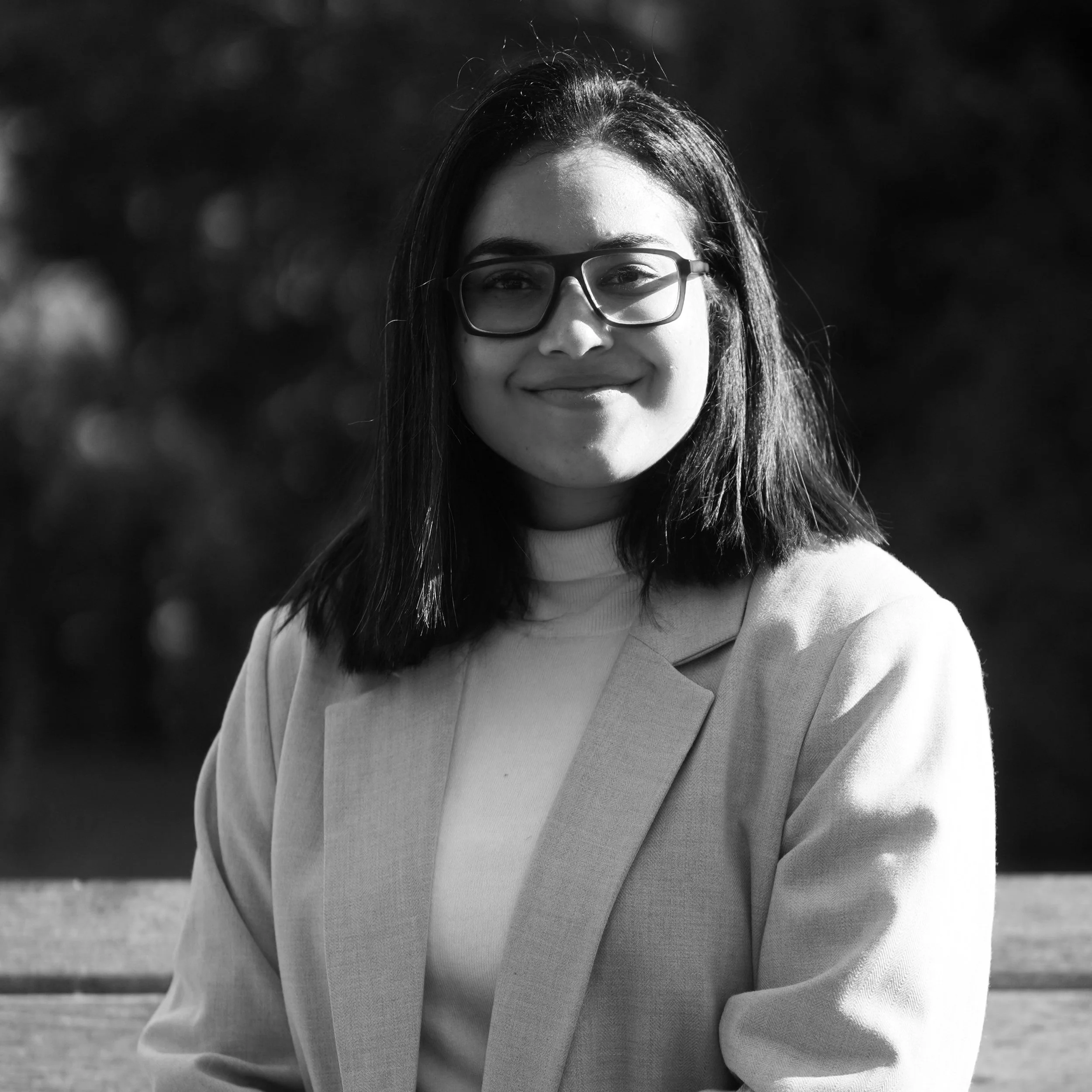 Smiling person with glasses wearing a blazer, black and white photo