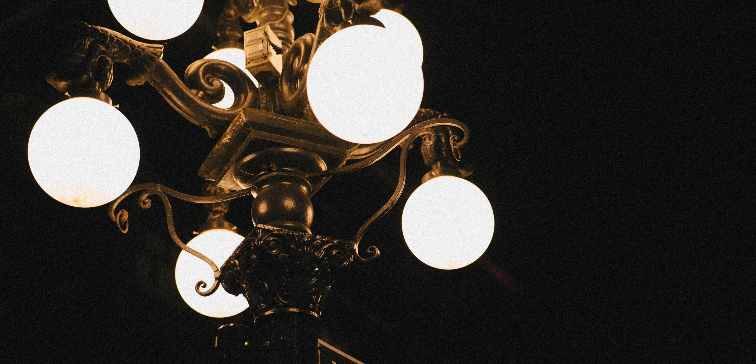 Ornate street lamp with multiple glowing round bulbs against a dark background.