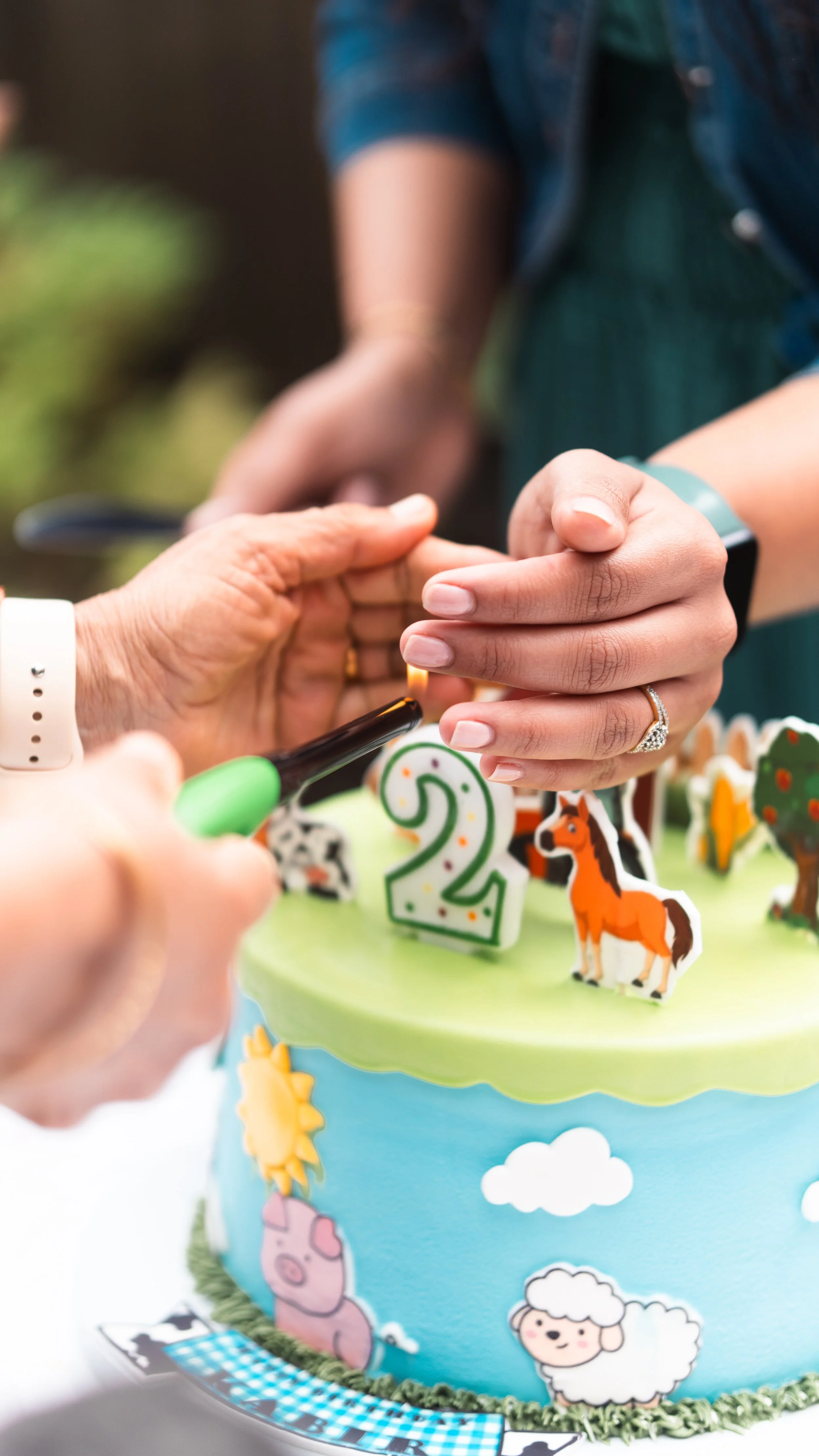 People lighting a candle on a farm-themed birthday cake with a number 2 candle.