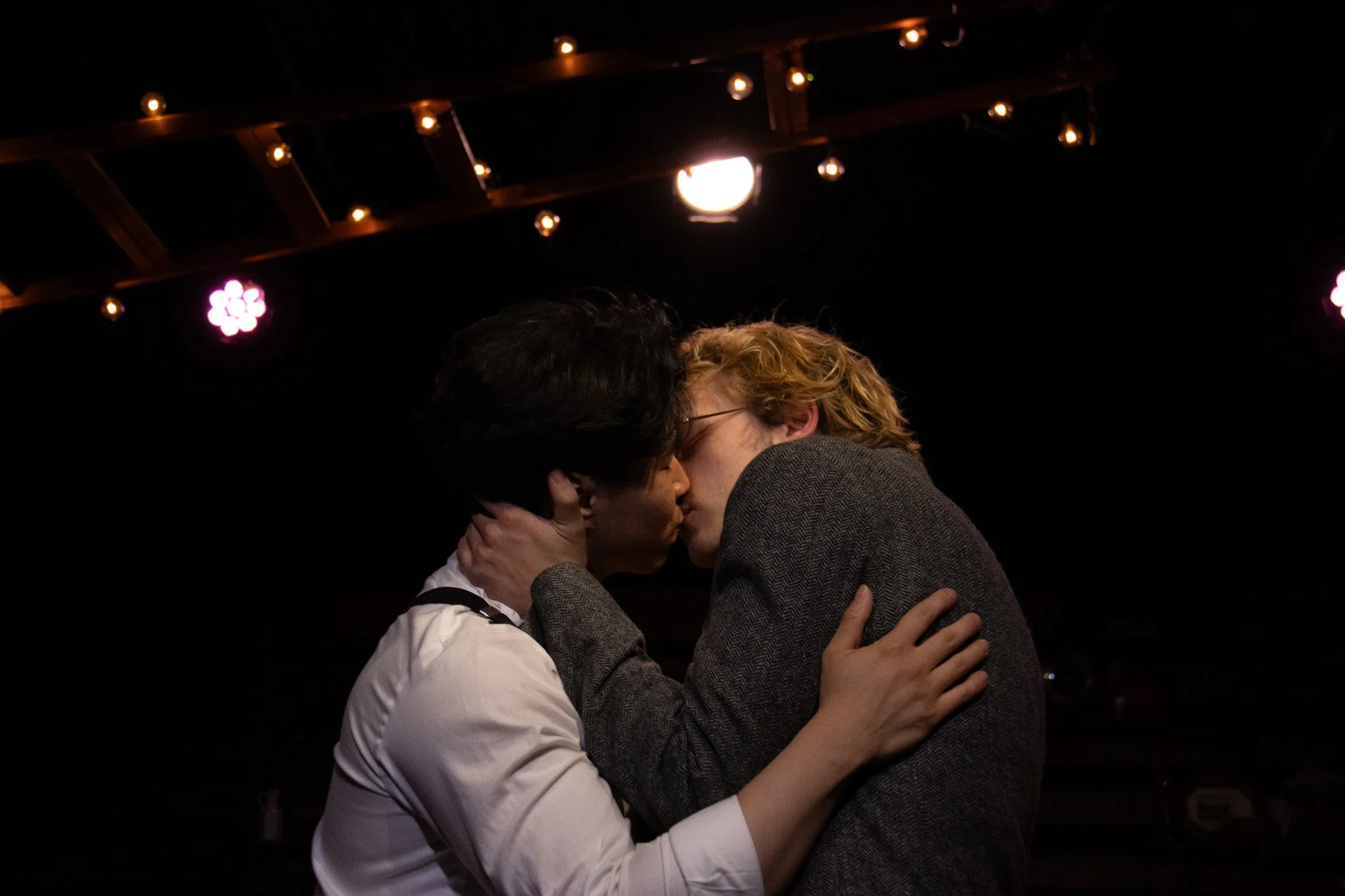 A couple sharing a kiss in a dimly lit setting with string lights overhead