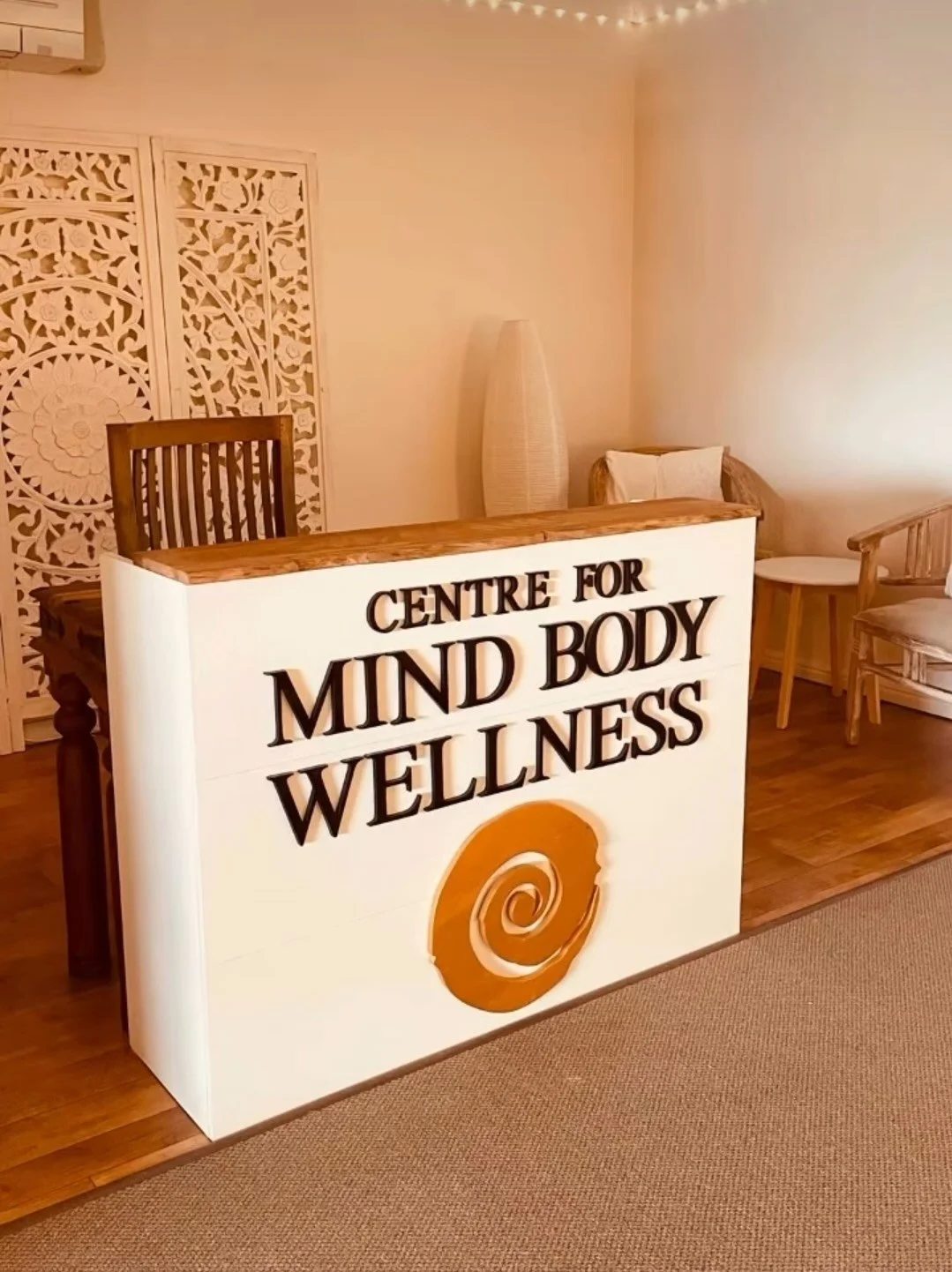 Reception desk with sign reading "Centre for Mind Body Wellness" in a cozy, nicely decorated interior.