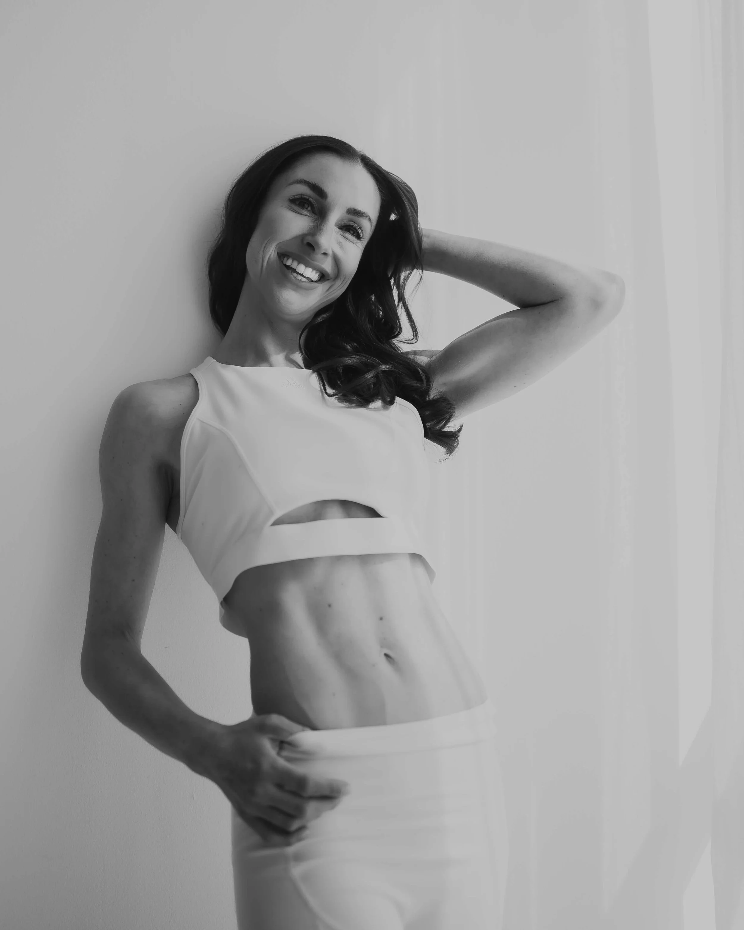 Smiling woman in workout attire posing against a wall in a black and white photo.