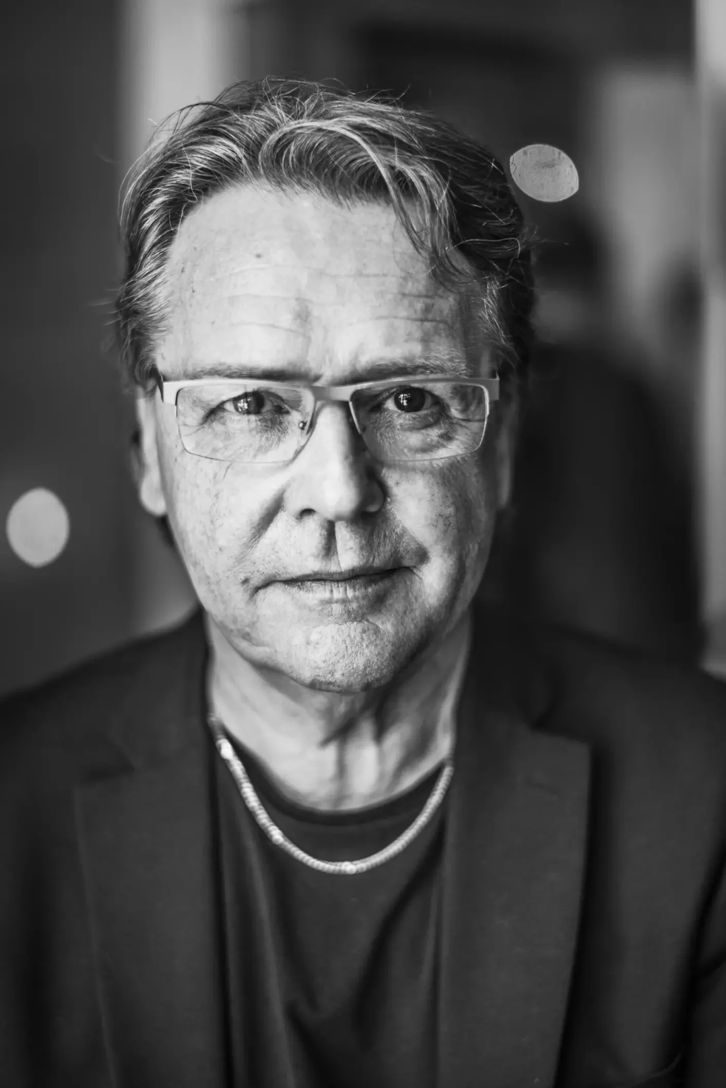 Portrett av en eldre mann med briller, iført mørk jakke og kjede, sett i svart-hvitt.