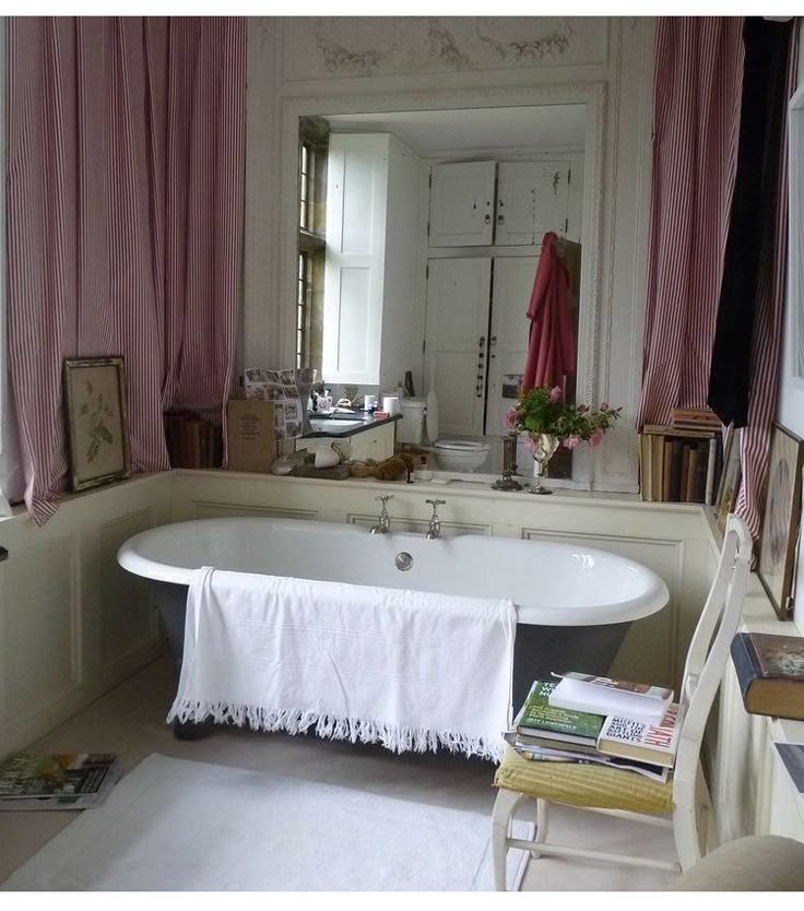 Vintage bathroom with freestanding bathtub, white towel, large mirror, and red striped curtains.
