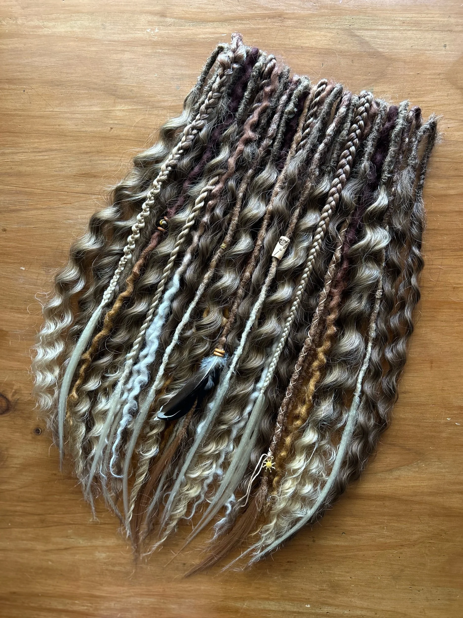 Collection of various styled and colored artificial hair extensions or dreadlocks arranged on a wooden surface.