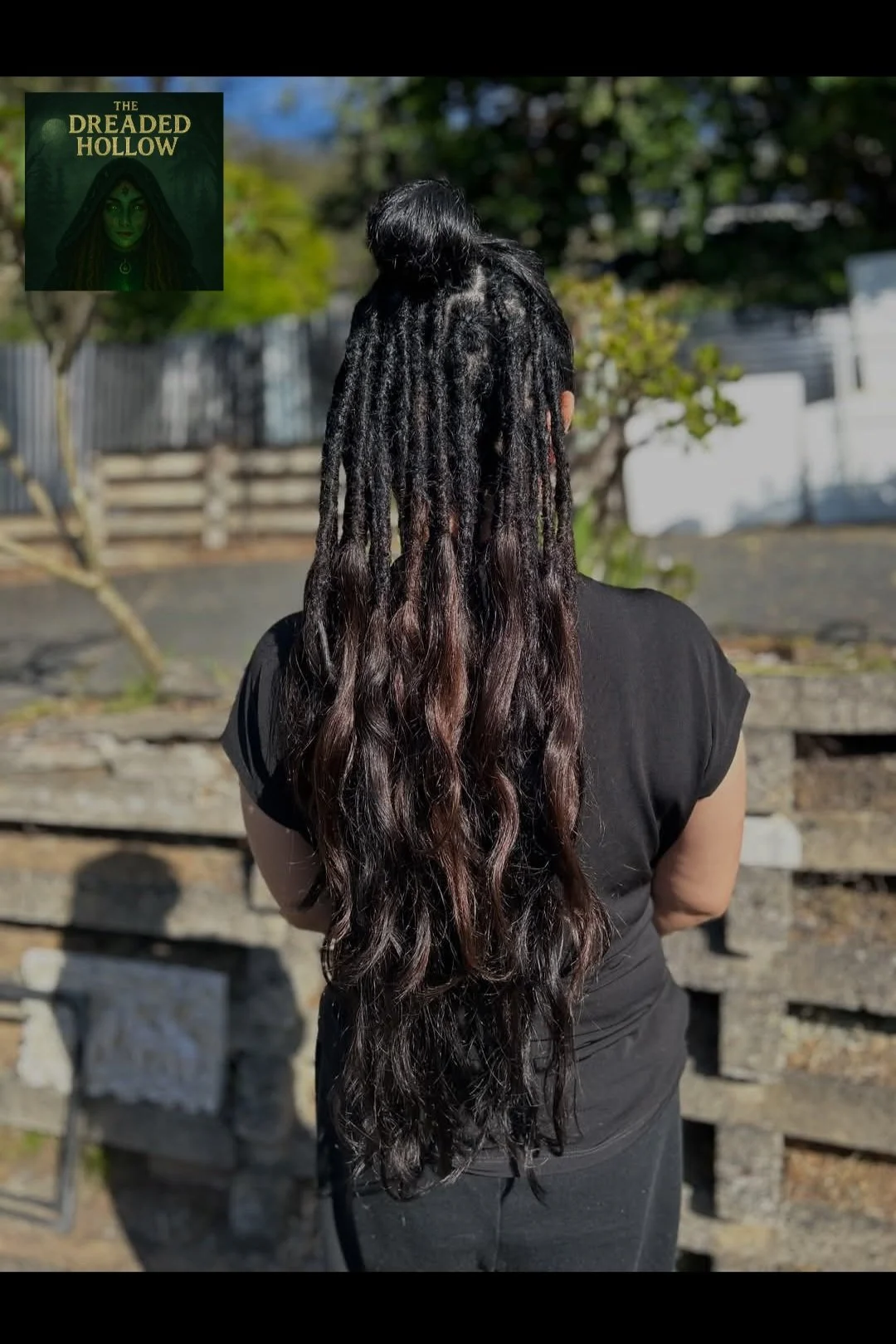 A woman with long dreadlocked hair standing outdoors with her back to the camera.