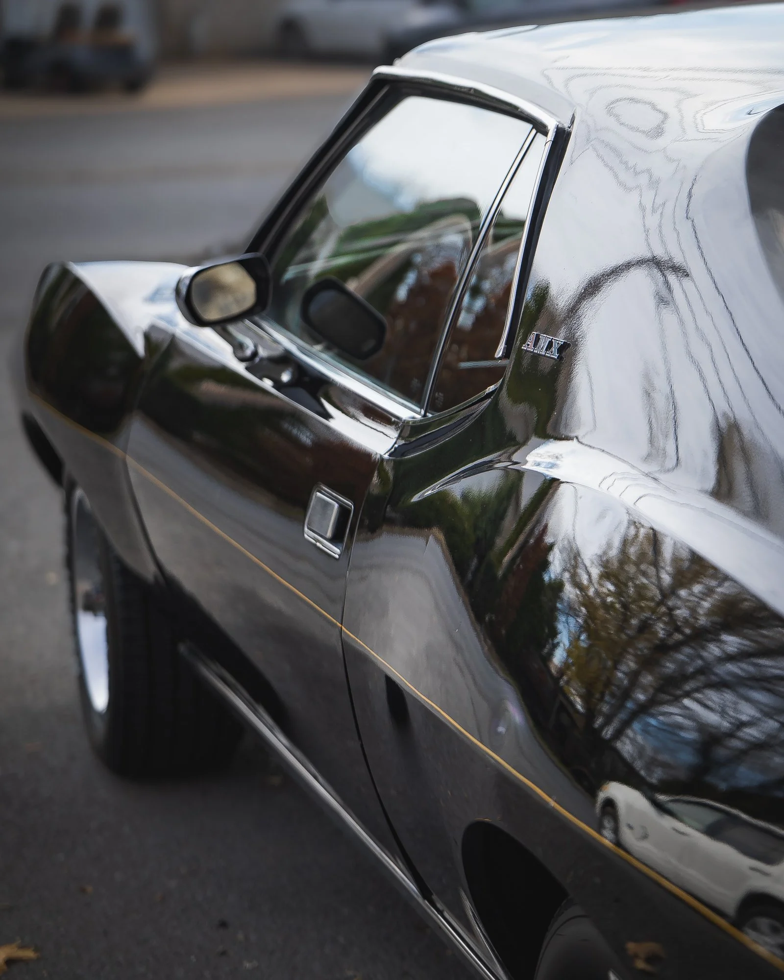 Close-up of a vintage black car parked outdoors with trees and sky reflections on its surface.