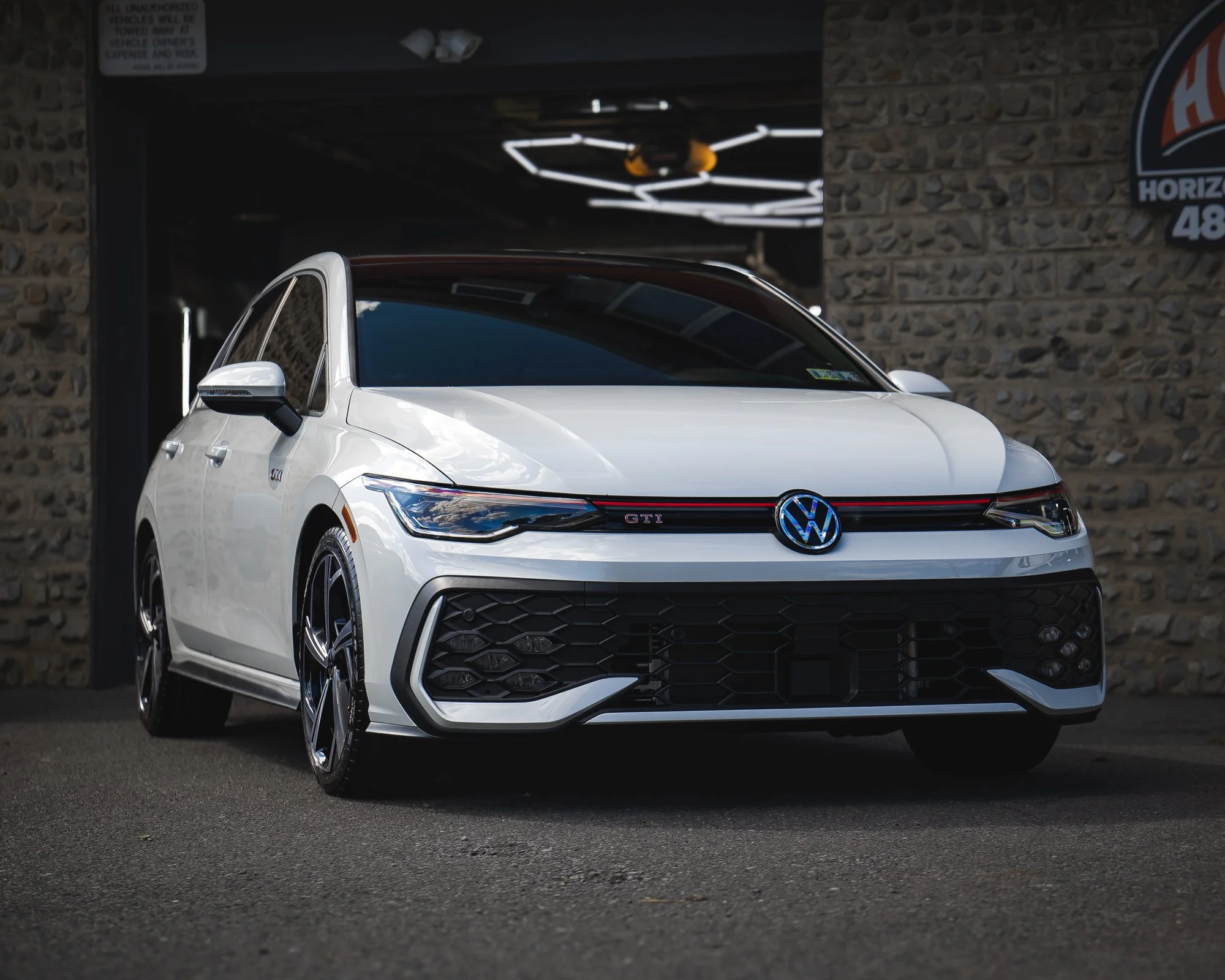 White Volkswagen GTI parked outside a building with a stone wall background.