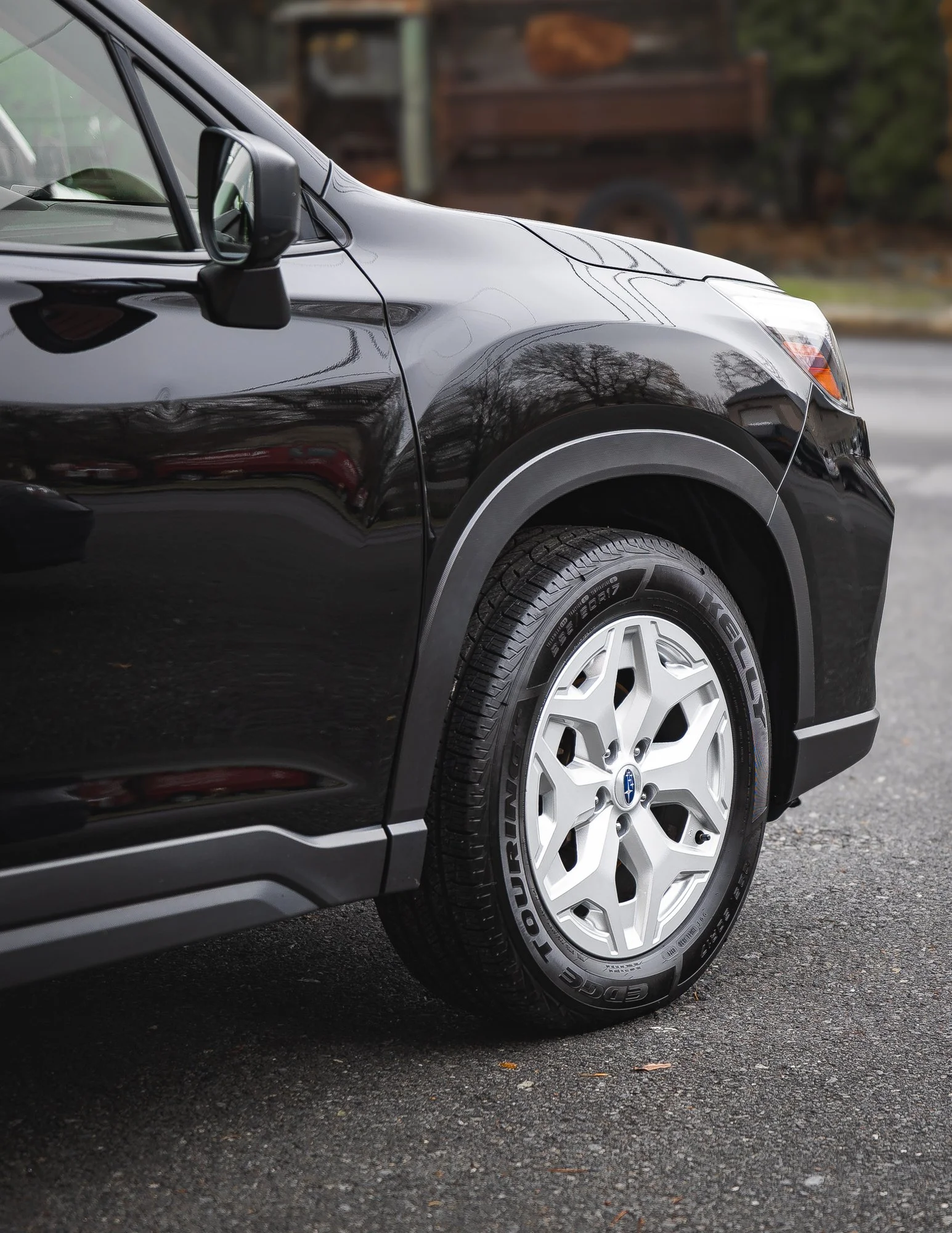Close-up of the front left side of a black Subaru SUV with white alloy wheel and tire, parked on the street.