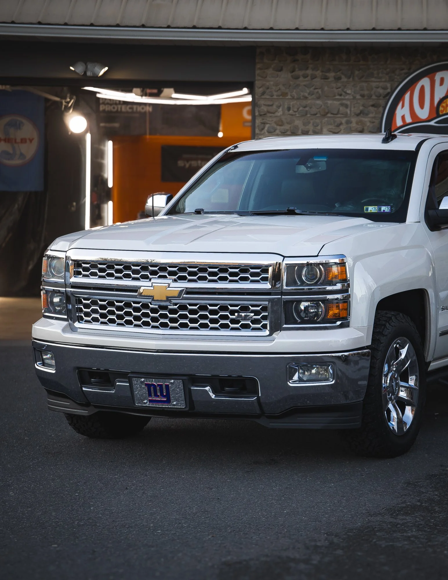 White Chevrolet Silverado pickup truck parked outside a building with signs in the background.