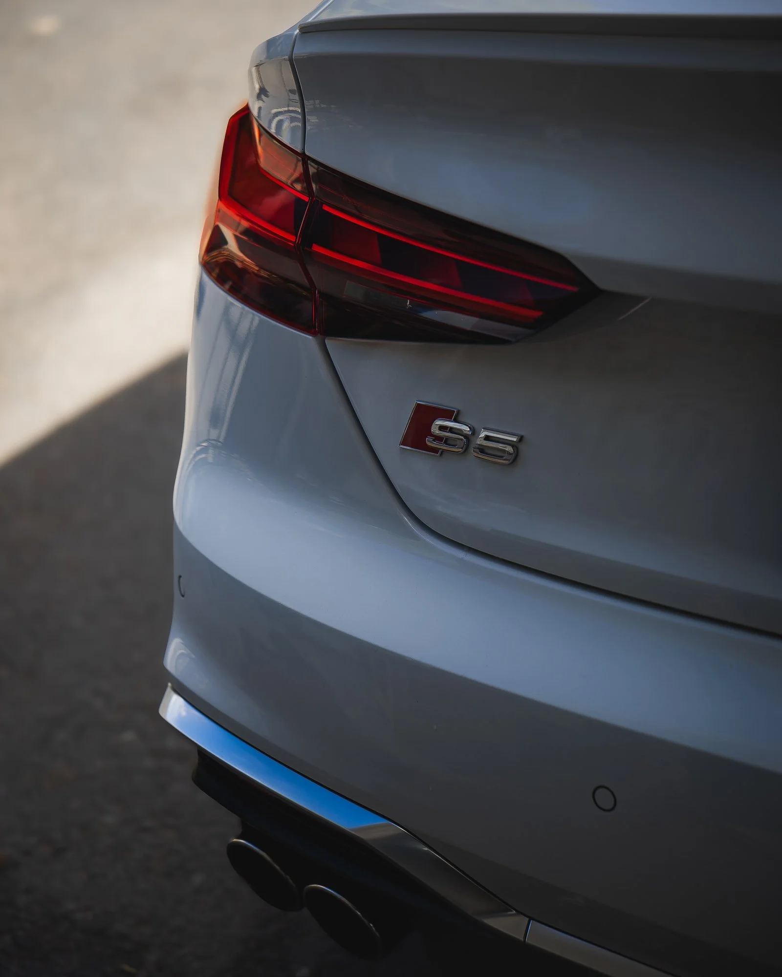 The rear of a silver Audi S5 car showing the taillight, part of the trunk, and the S5 badge.