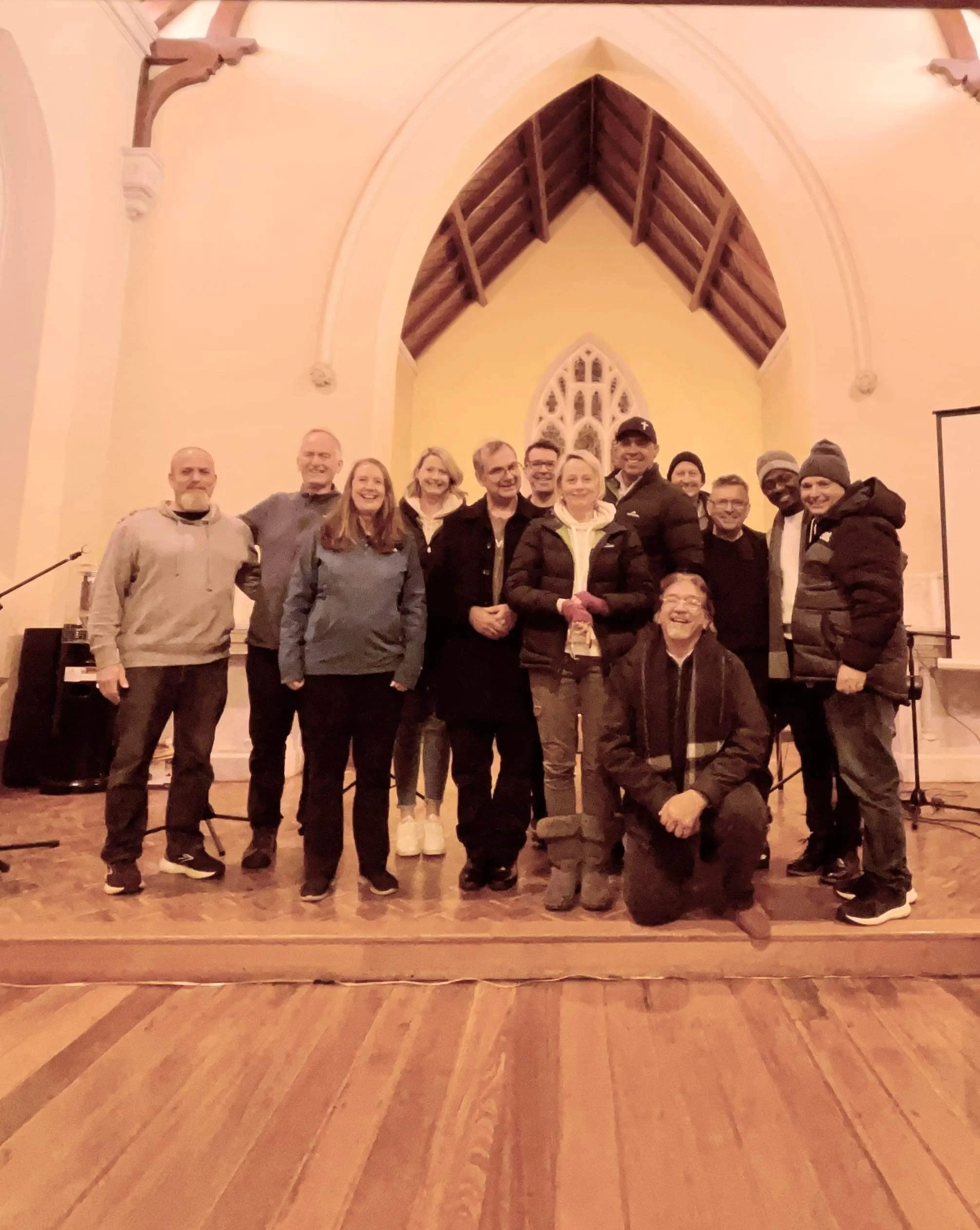 Group of people posing in a church with wooden floors and arched ceiling.