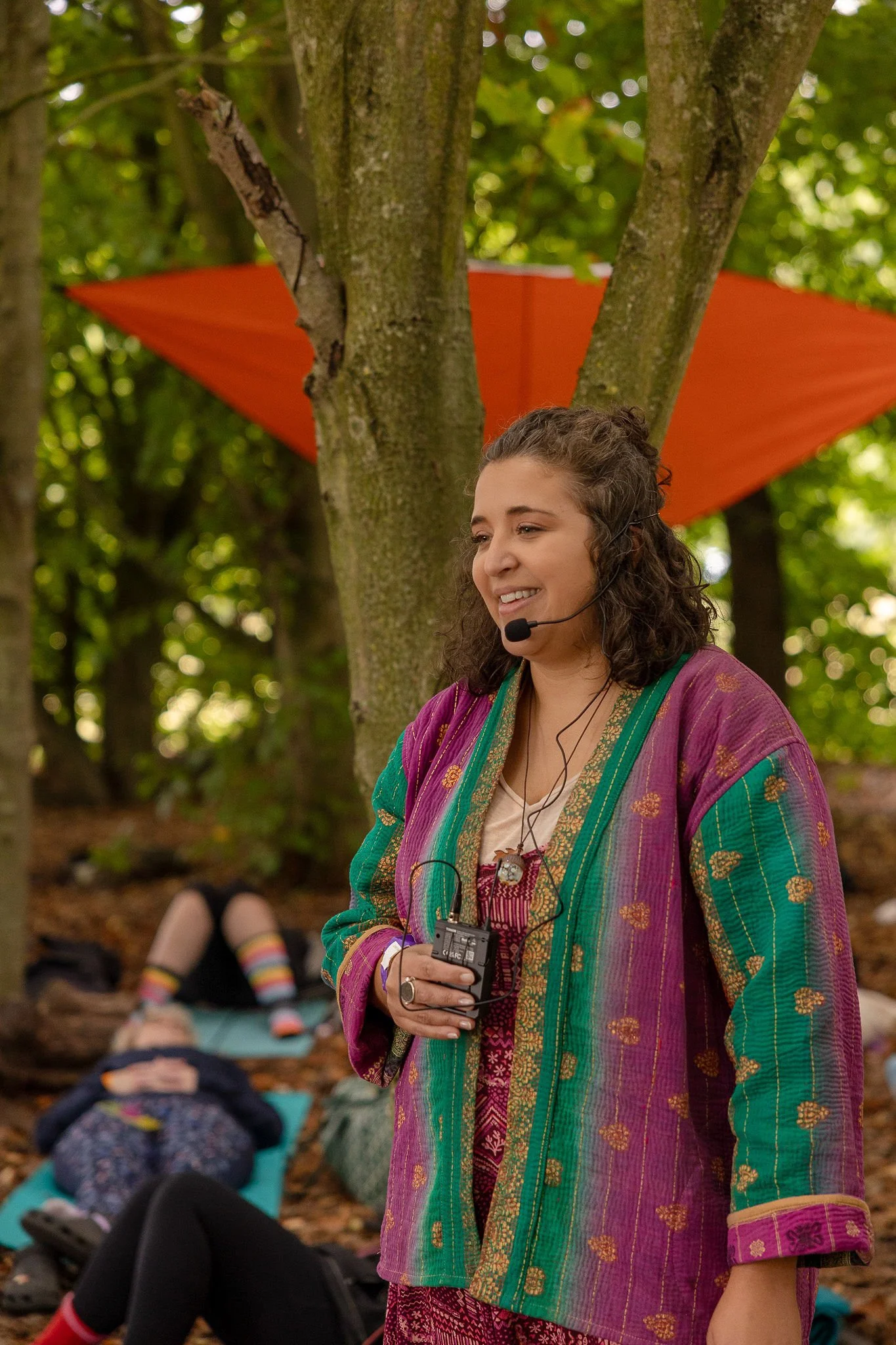 A smiling woman with shoulder-length curly hair sitting at a table with a colorful cloth, two large candles and a white crystal in front of her, with a decorative mirror and chandelier in the background.