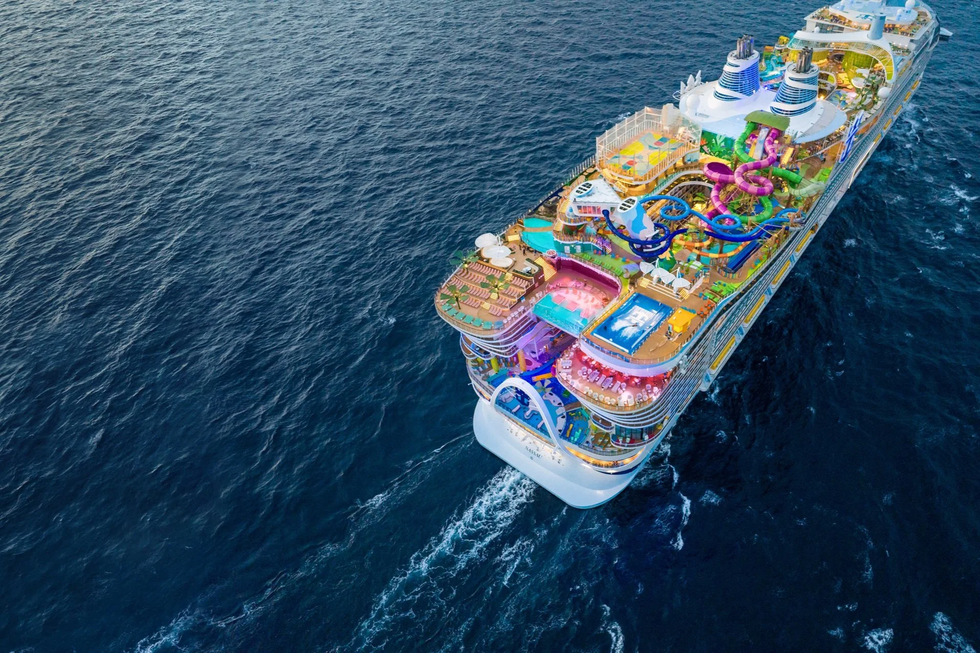 Aerial view of a colorful cruise ship with multiple swimming pools and water slides sailing on the ocean.