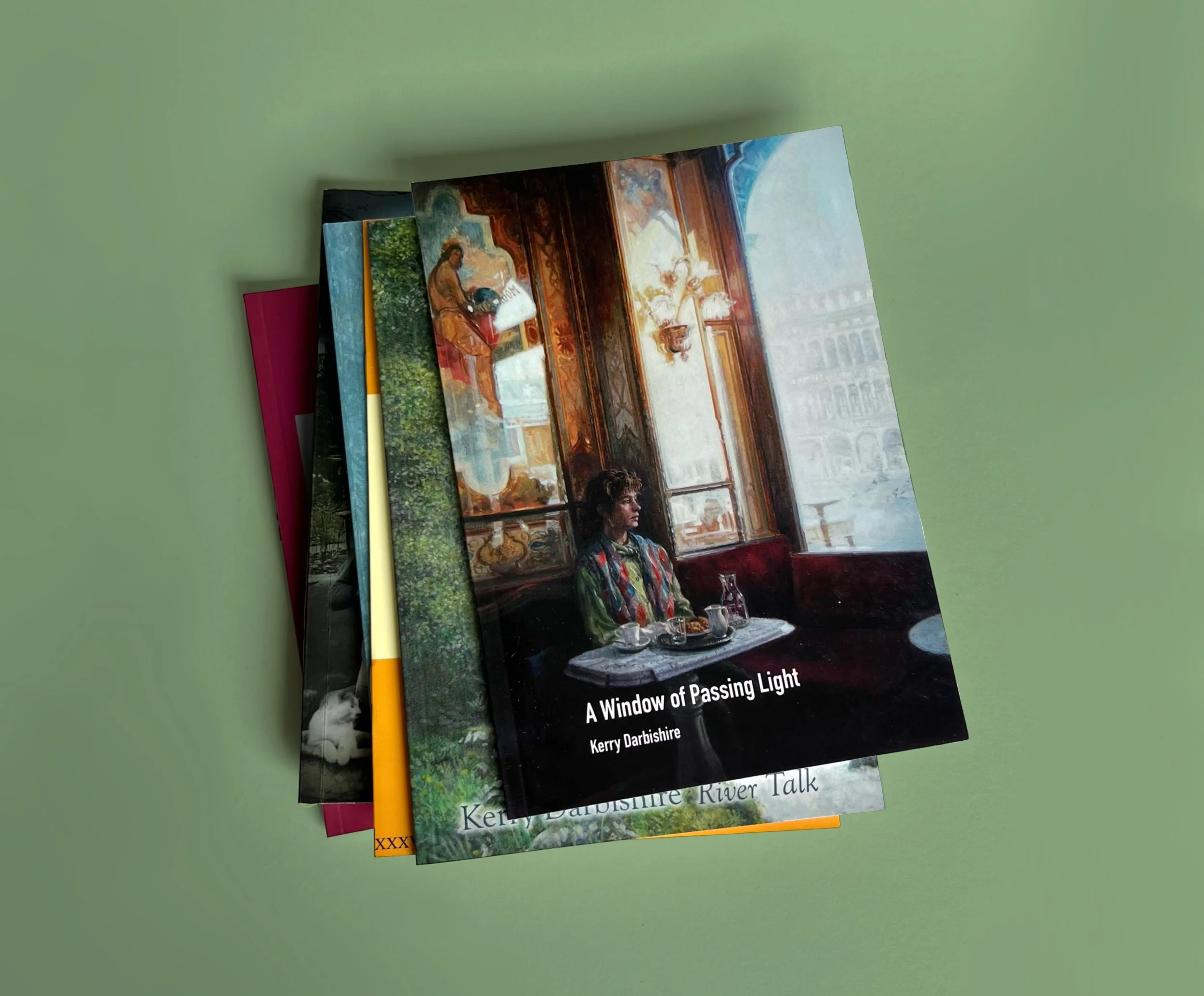 A stack of colorful books with the top book titled "A Window of Passing Light" by Kerry Darbeshire, featuring a cover illustration of a woman sitting at a table near a large window with sunlight streaming in.