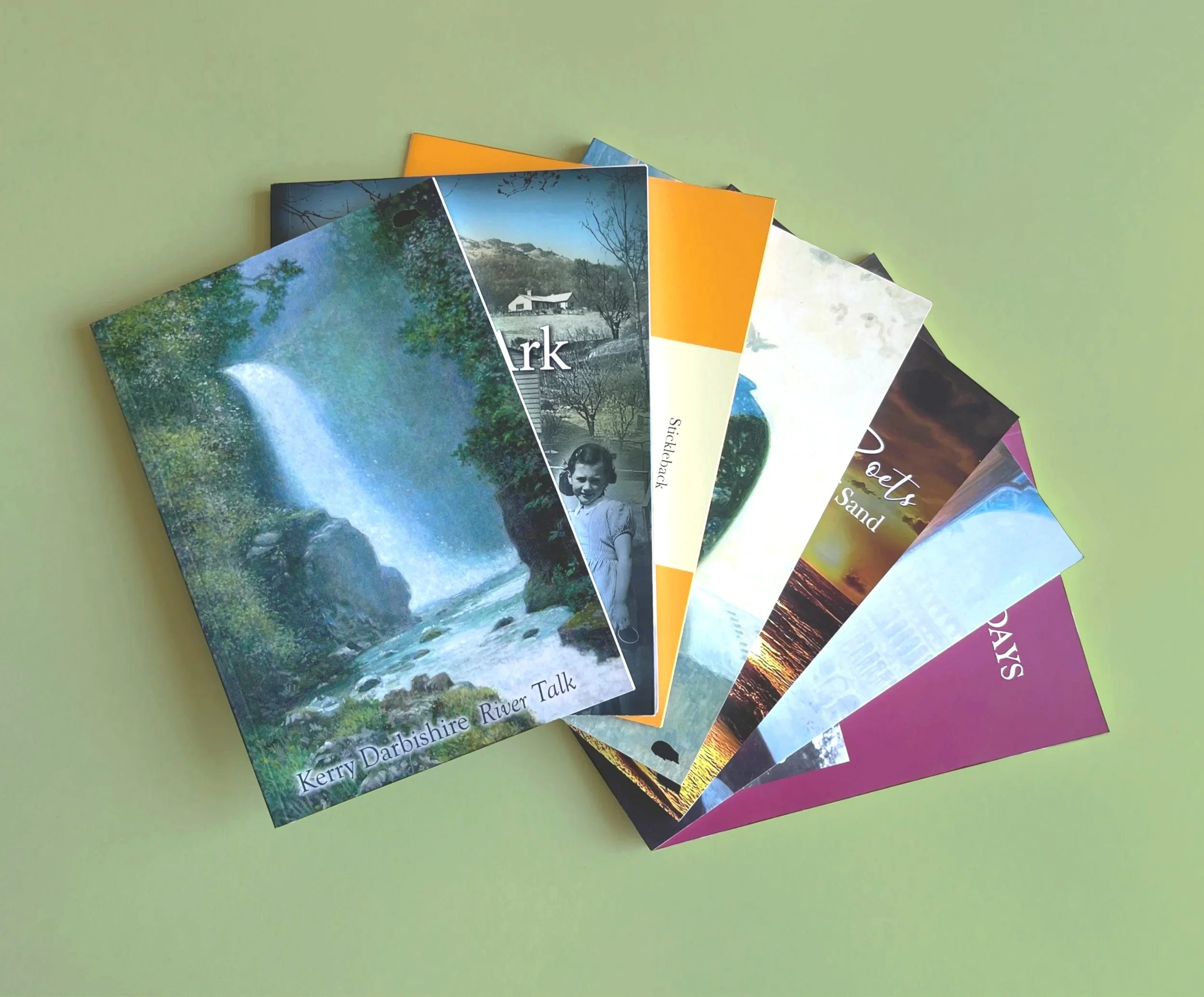 A collection of colourful poetry books spread out on a light green surface, featuring nature scenes and photographs.