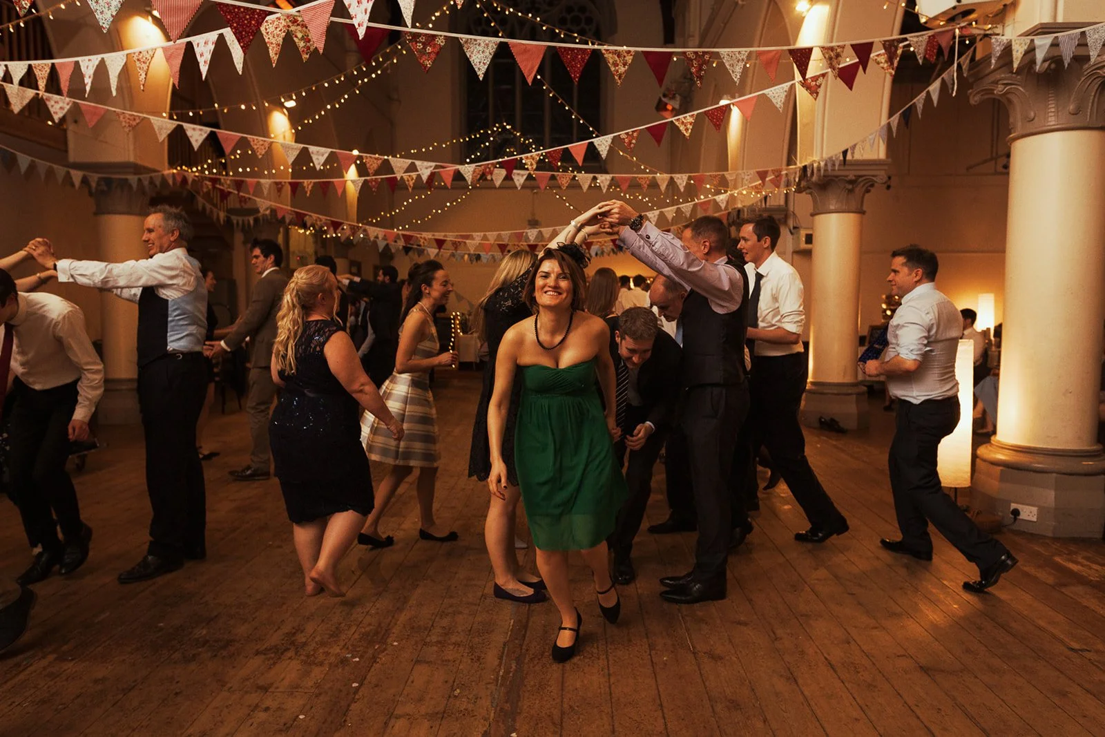 People dancing and having fun at a celebration party with bunting decorations and warm lighting.