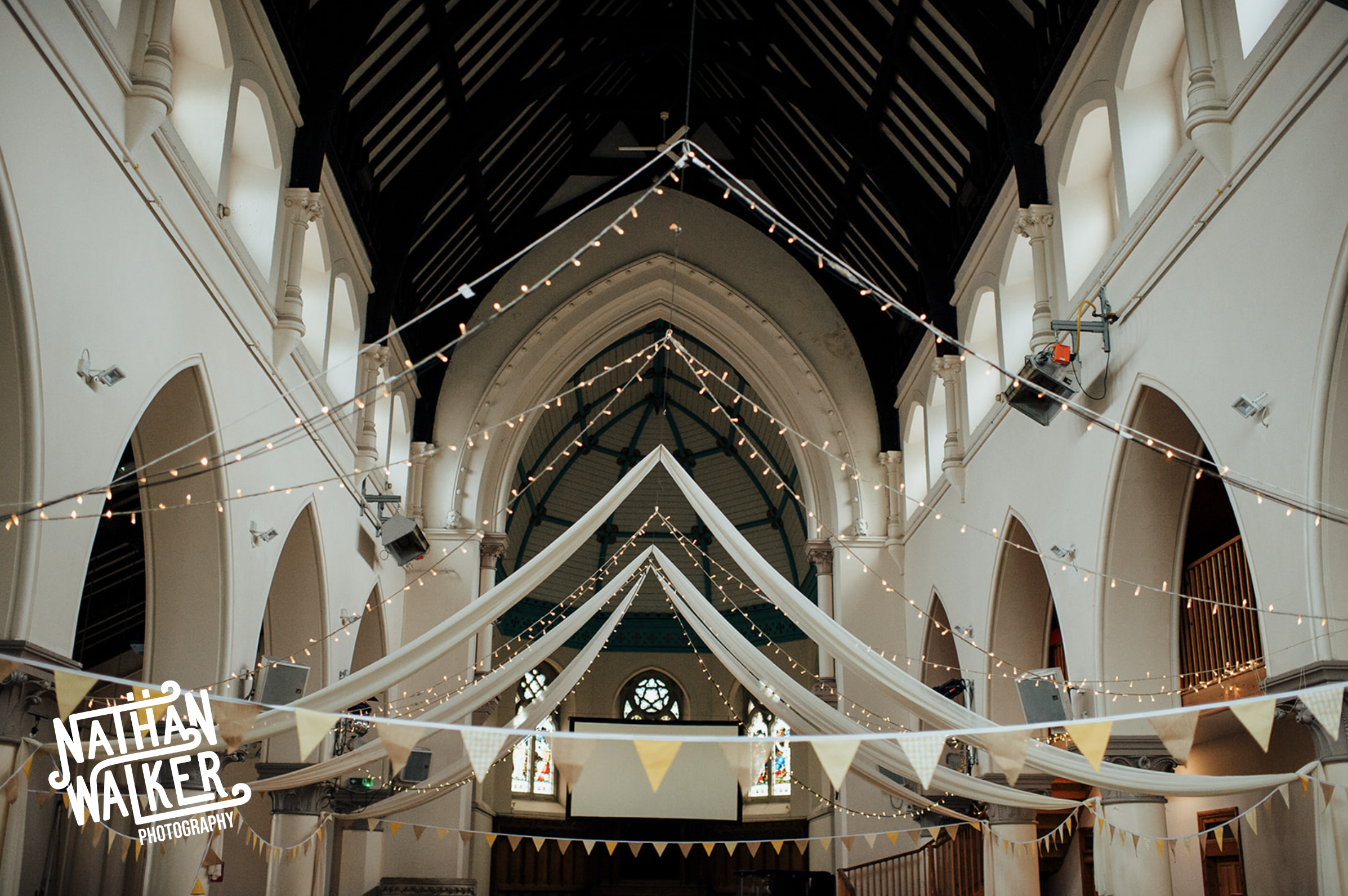 Decorated church interior with white fabric drapes and strings of fairy lights hanging from the ceiling, and bunting banners in white and yellow.