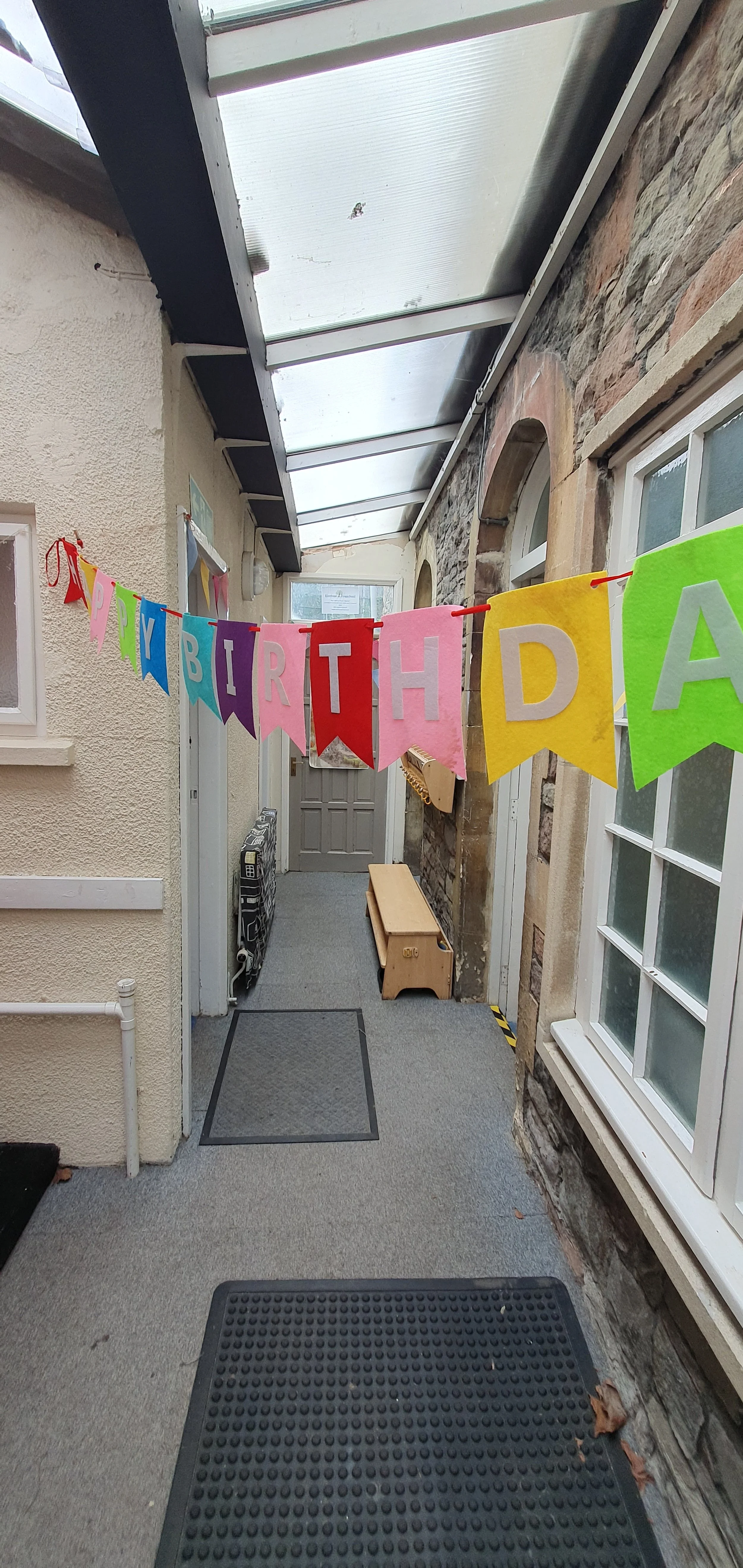 Outdoor covered walkway decorated with colorful birthday banners, small bench, and storage units.