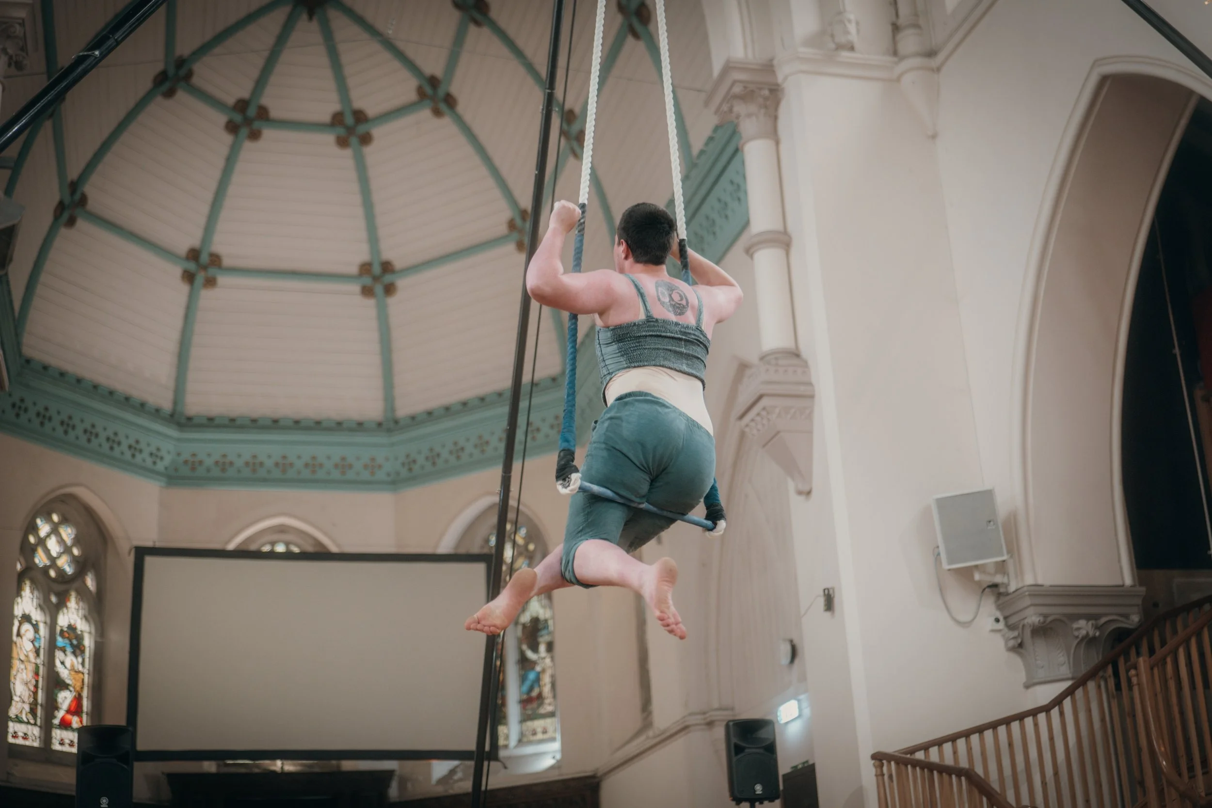 A performer swinging on a trapeze inside a church with stained glass windows.