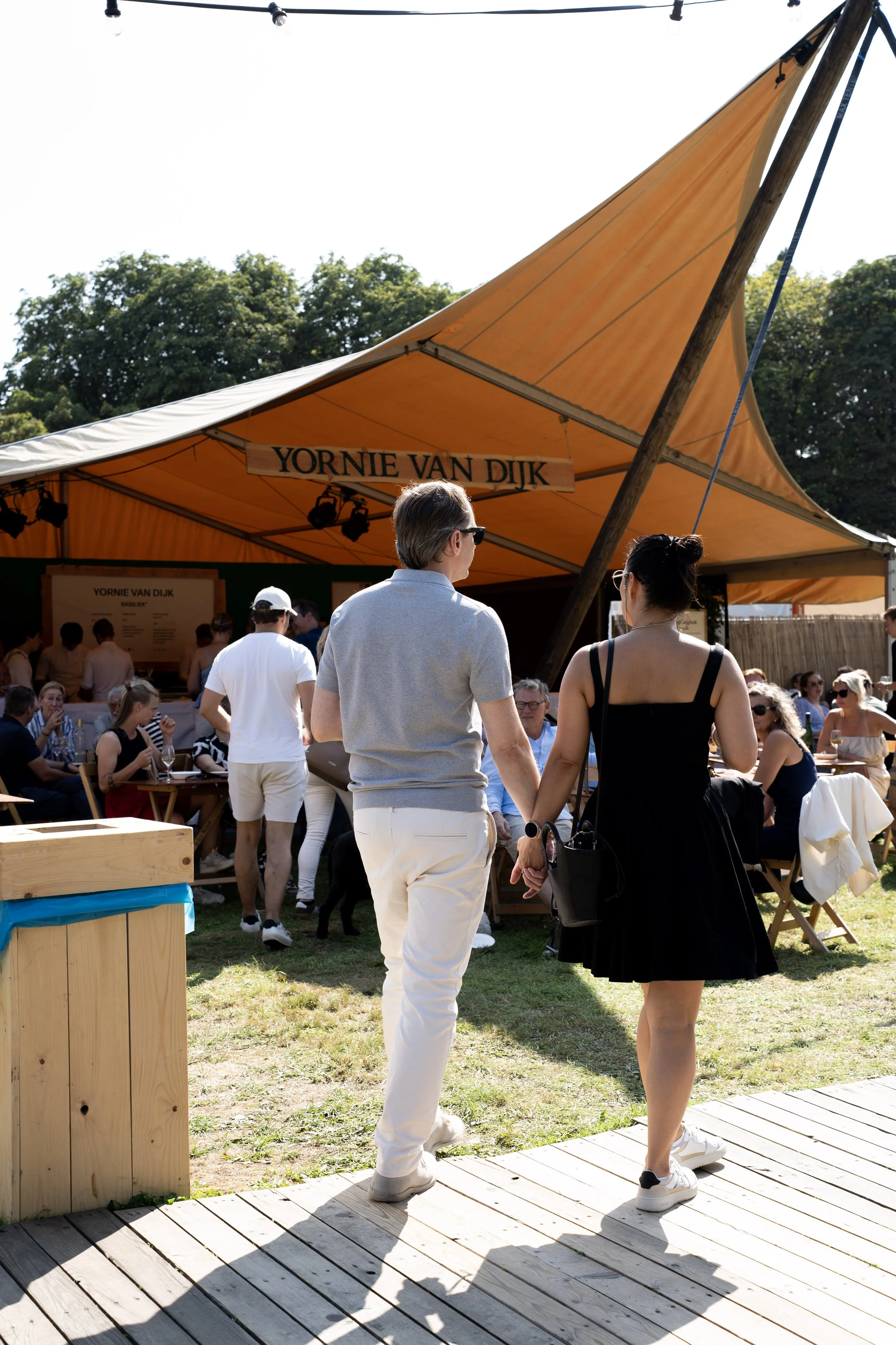 Mensen genieten op een zonnig terras met een gele tent met de tekst 'Yornie Van Dijk'.
