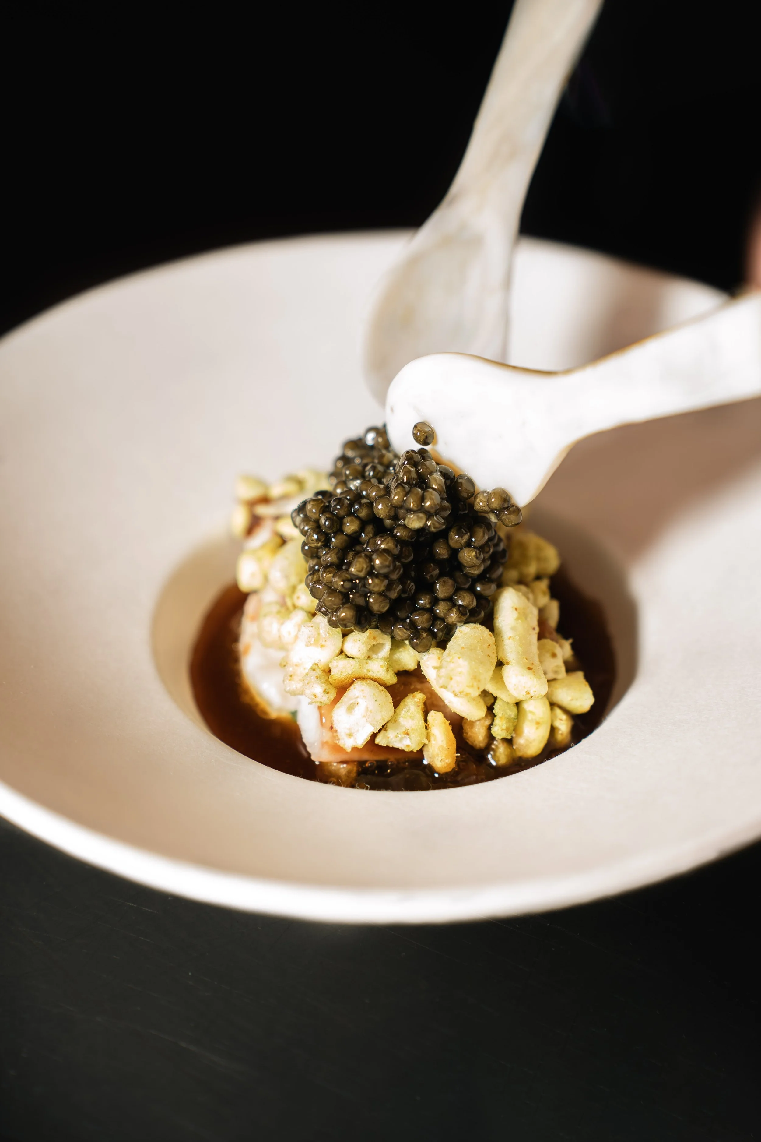 Gepresenteerd dessert met zwarte kaviaar, crèmepoeder en andere fijne ingrediënten in een witte kom.
