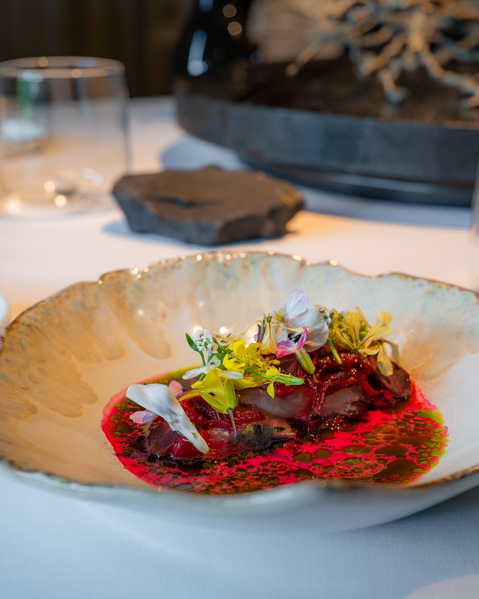 Gerecht met rood saus, belegd met diverse microgroenten en eetbare bloemen in een diepe gouden kom.