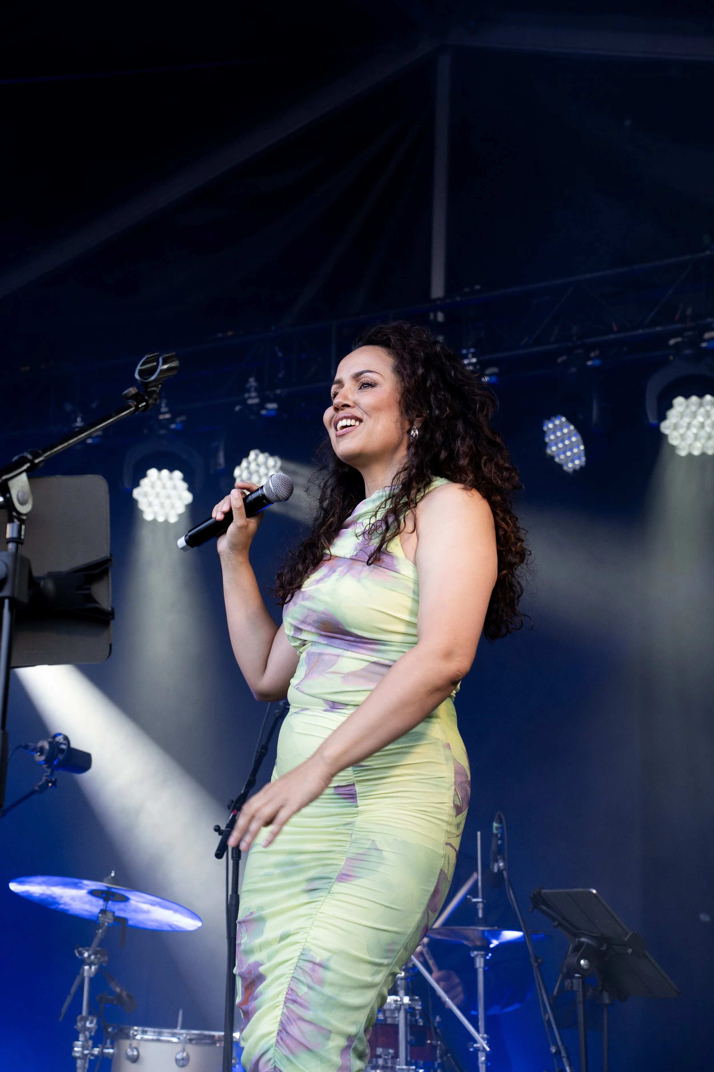 Een vrouw zingt op een podium, terwijl ze een microfoon vasthoudt, omringd door muziekinstrumenten en podiumverlichting.