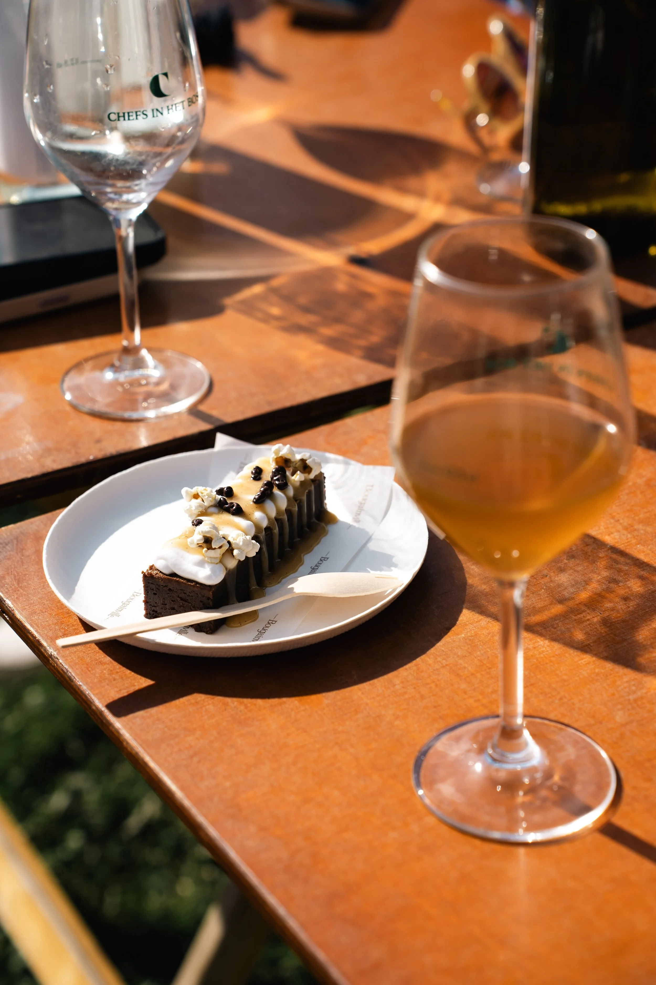 Een dessert op een wit bord naast twee wijnglazen met witte wijn op een houten tafel.