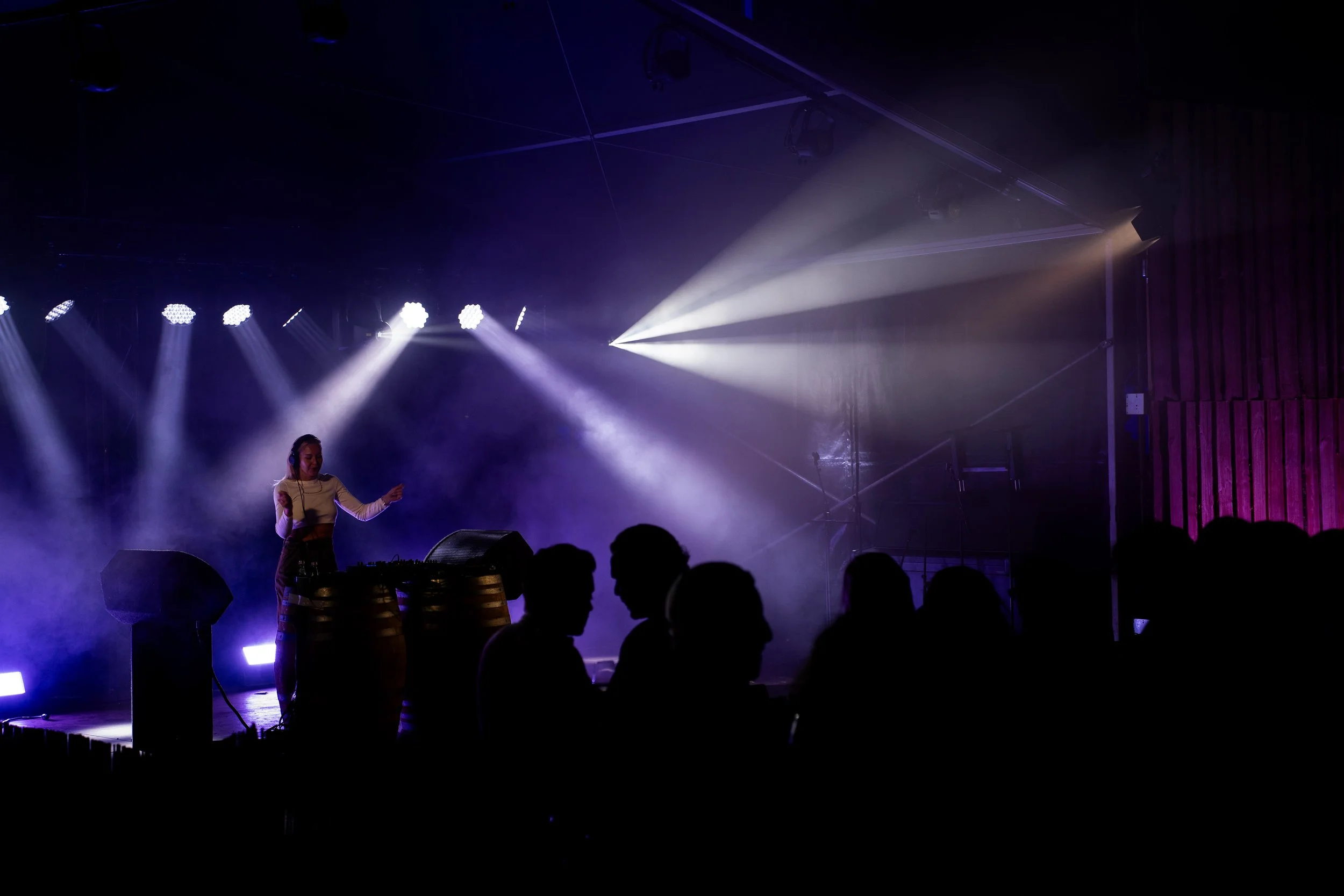 Een podium met dj's en lichteffecten tijdens een muziekoptreden met silhouet van publiek in de voorgrond.