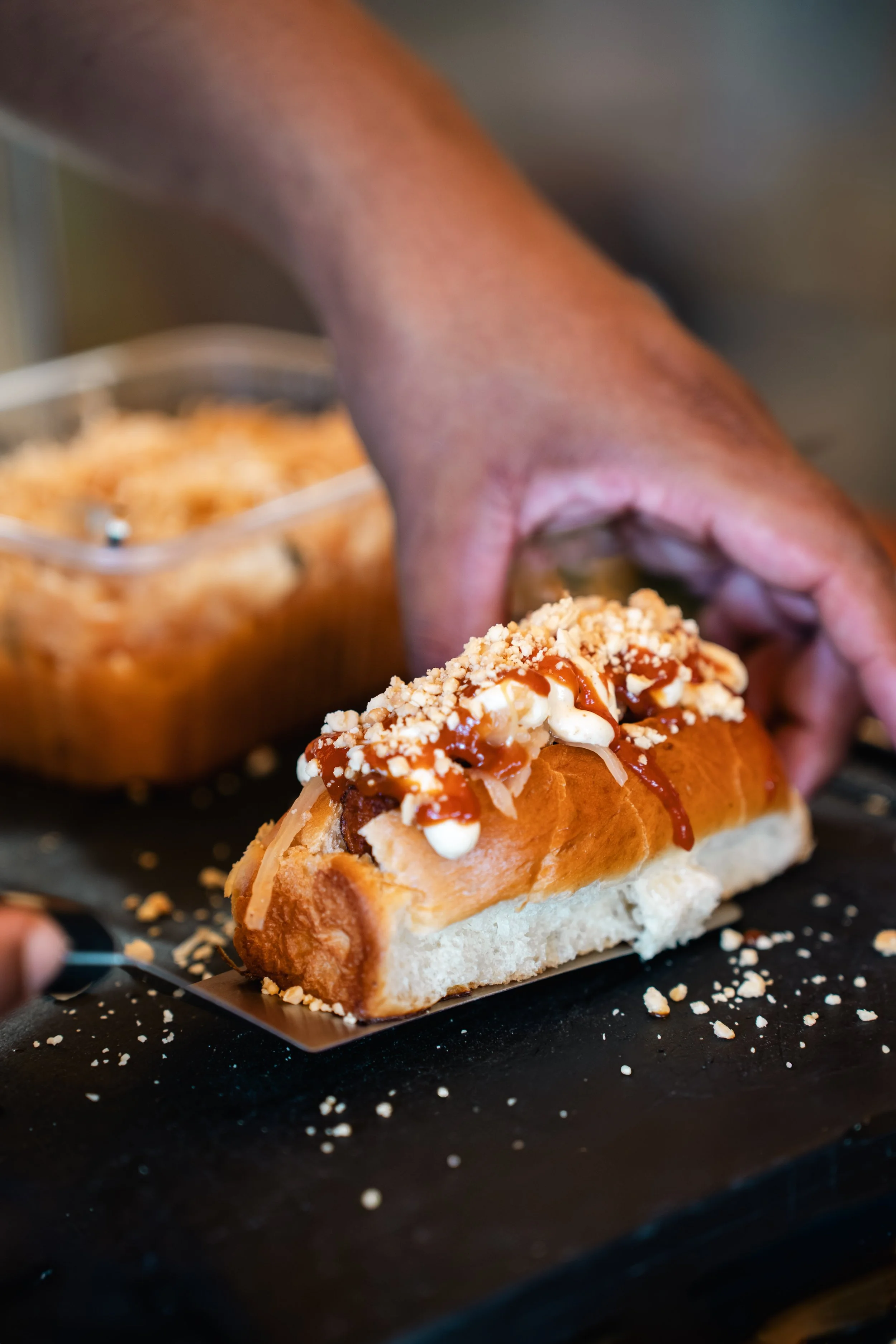 Close-up van een hotdog met ketchup, mayonaise, kaas, en saus, terwijl iemand het vult.