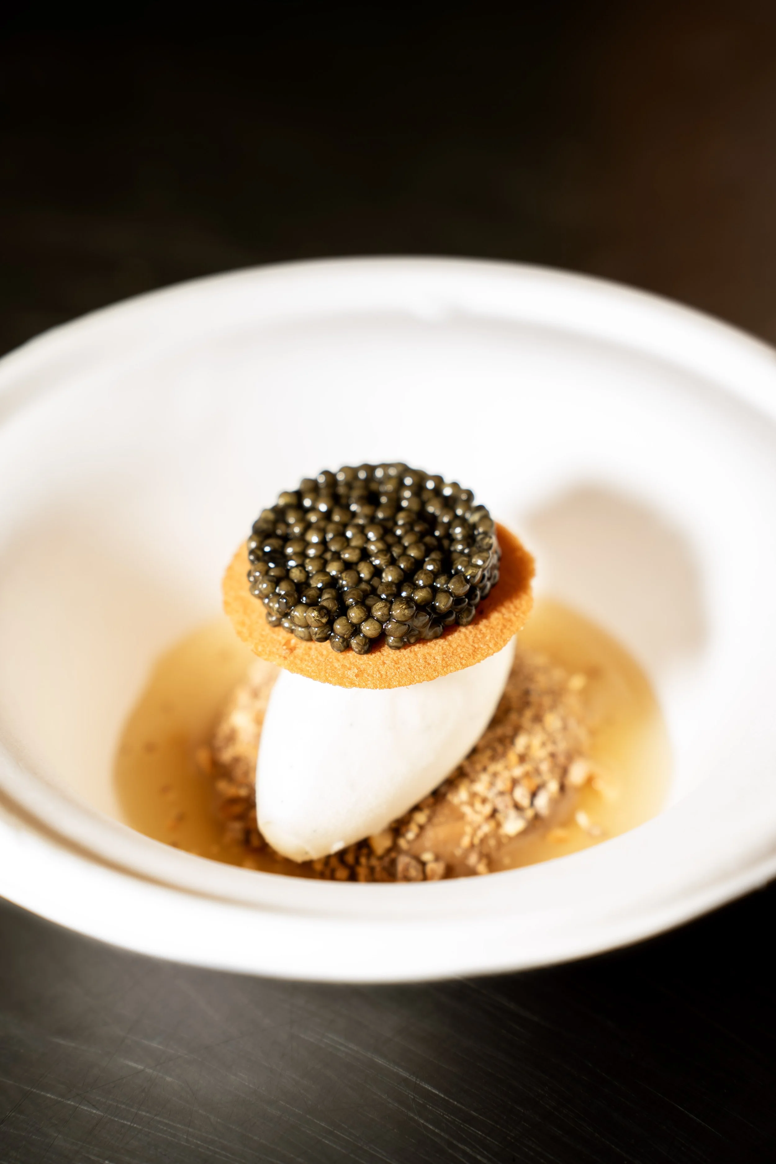 Een fijn gedetailleerde dessert met caviare, witte room, een oranje biscuit en een krokante bodem, geserveerd in een wit kommetje.