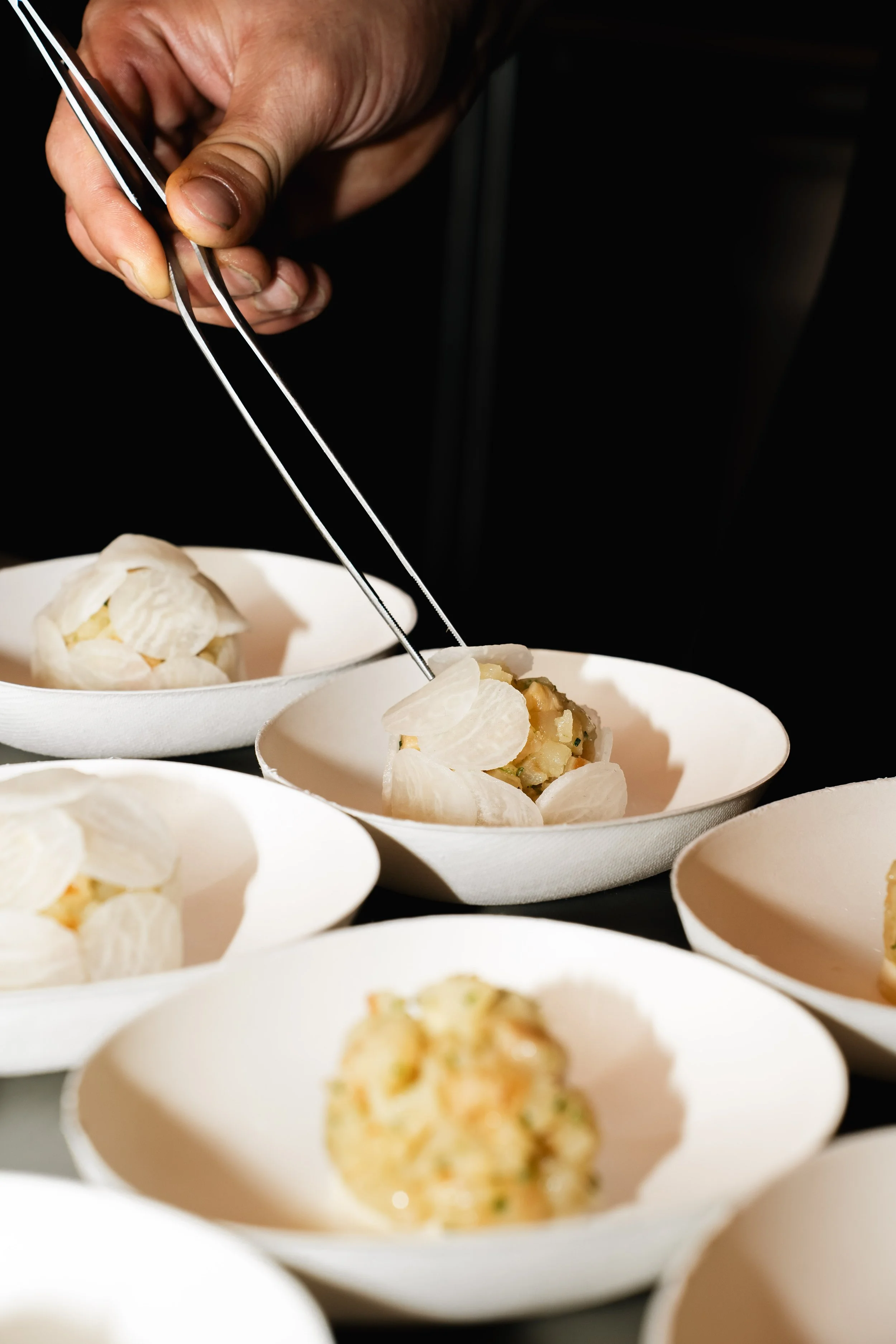 Hand pakt een eetlepel met voedsel uit een witte schotel met gerecht met aardappel en groenten.