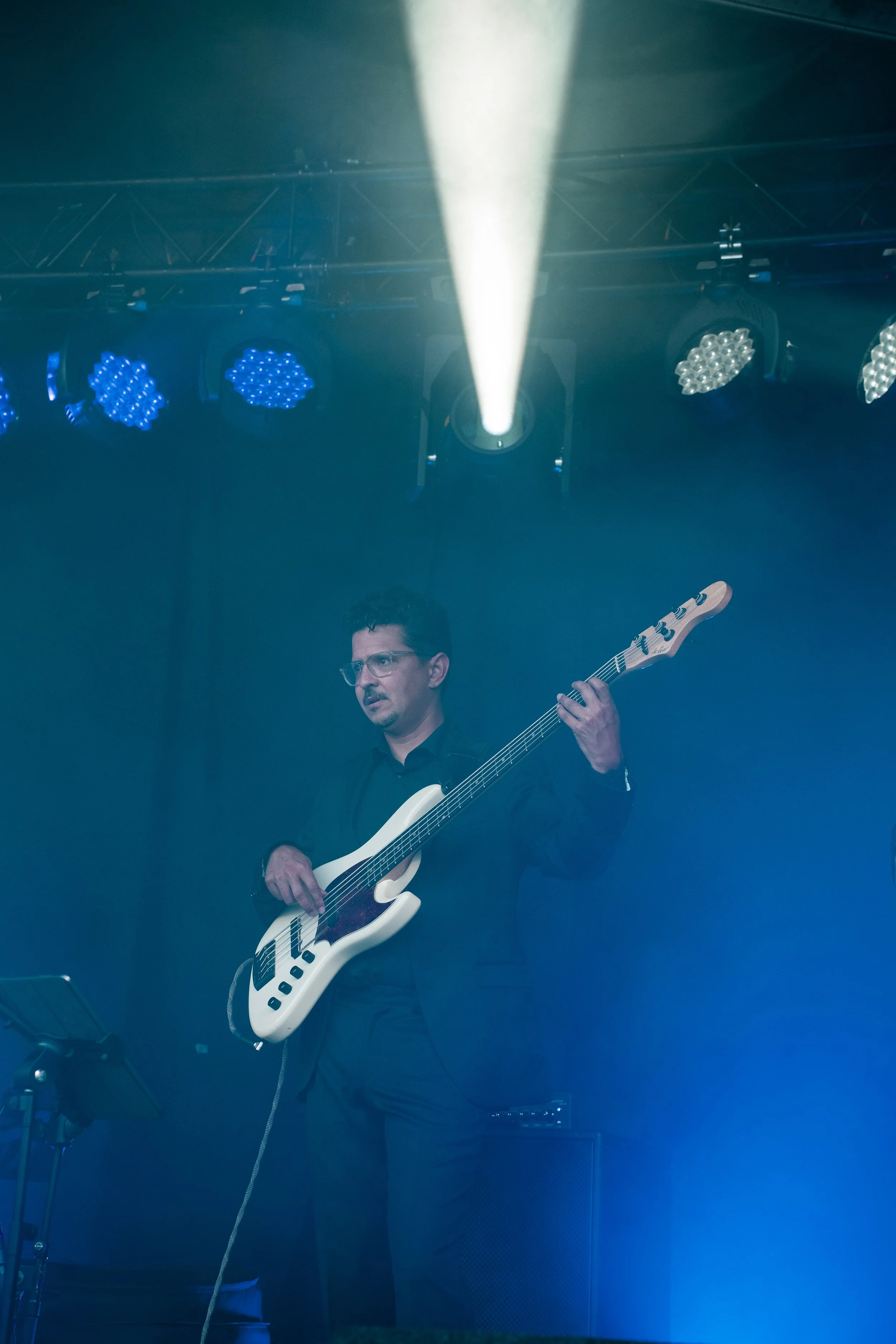 Man speelt elektrische basgitaar op een podium met blauwe en witte stageverlichting.