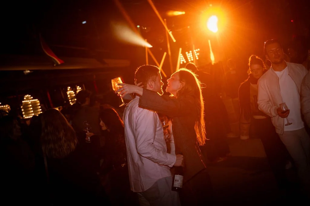 Mensen dansen en praten bij Amsterdam Wine Festival met felle, warme verlichting.