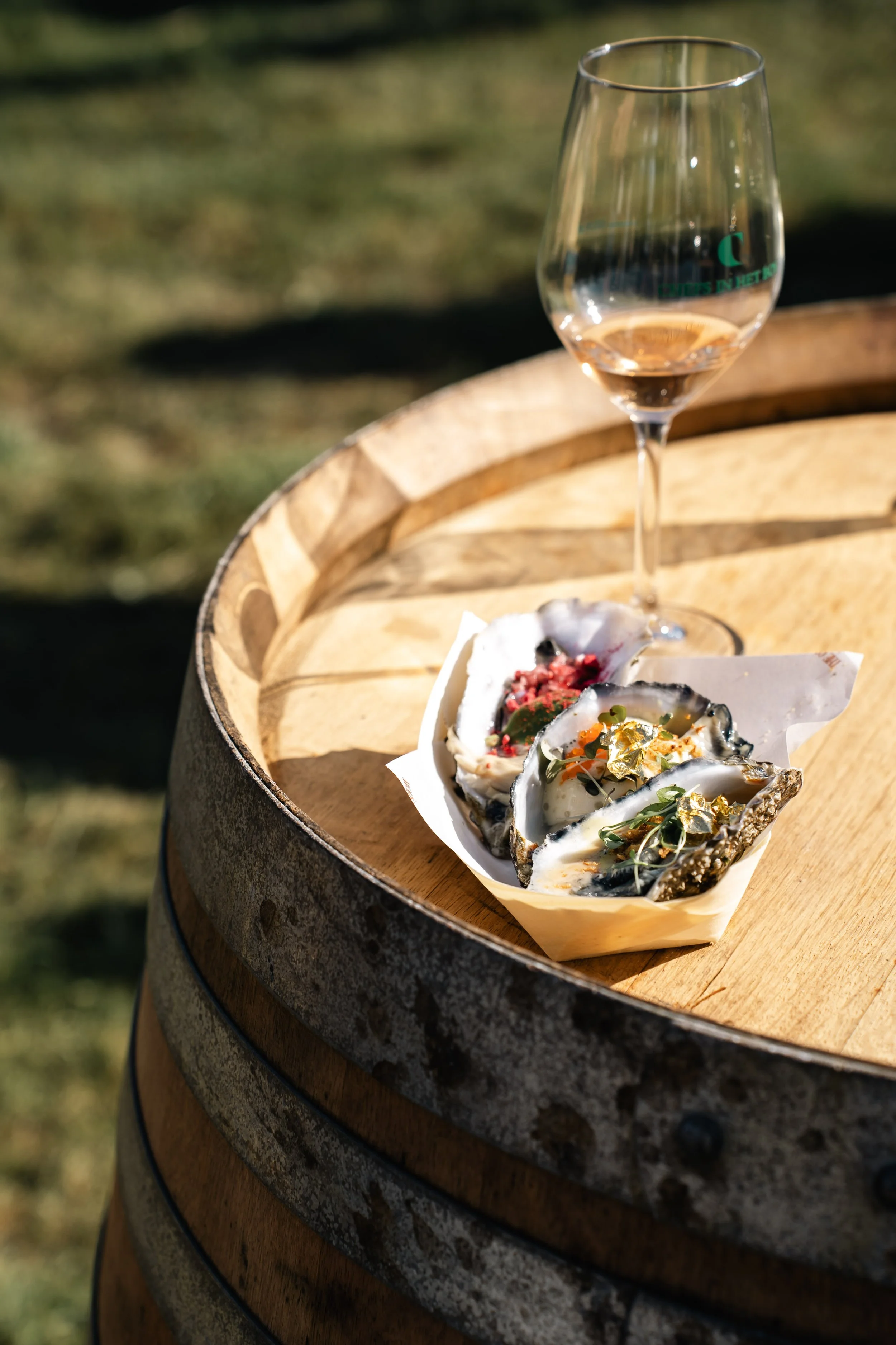 Glas rosé wijn op een houten vat met oysters en goudkleurige bladgoud versiering in de schelpen, buiten op het gras.
