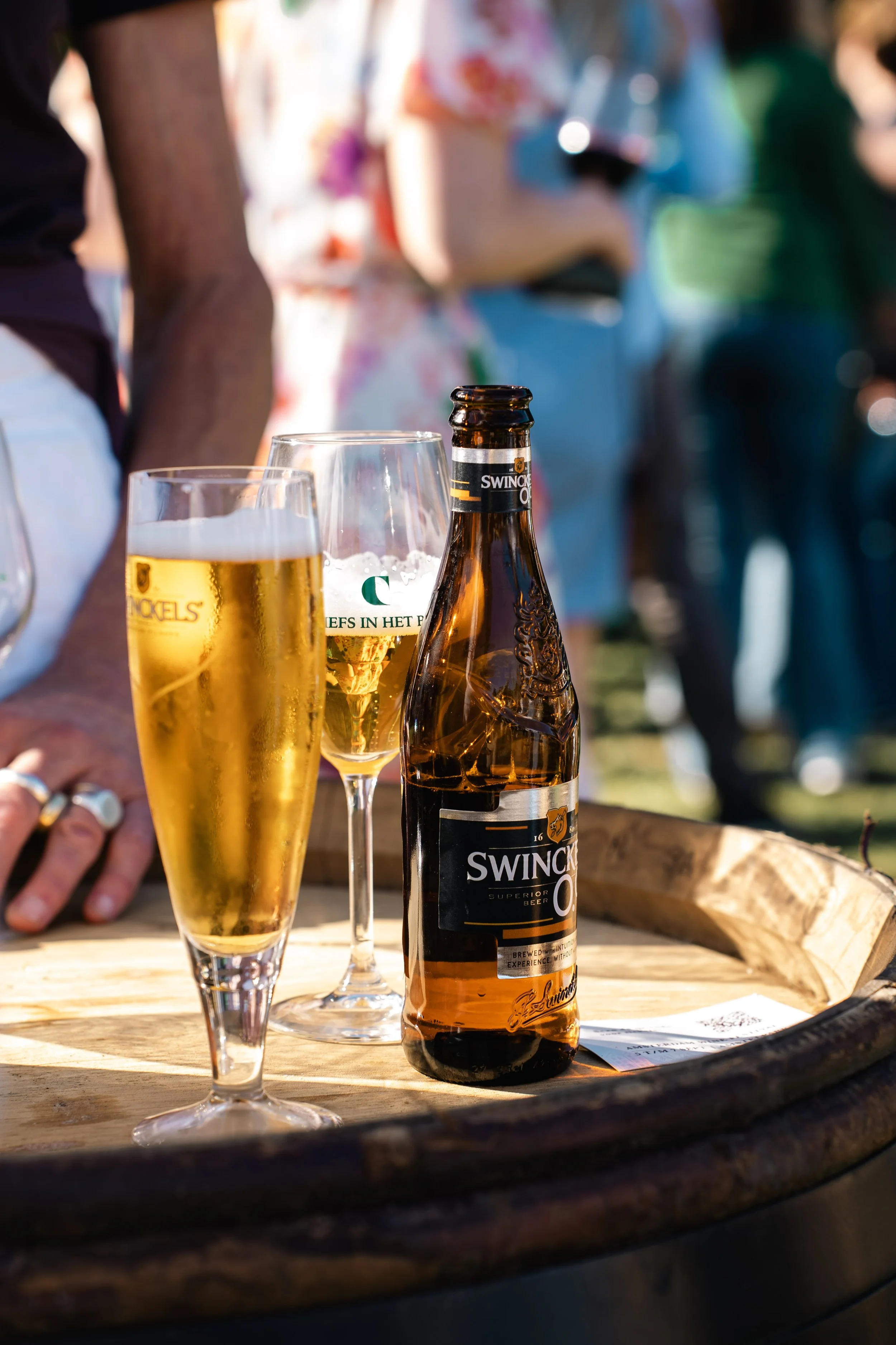 Bierflessen en glazen met bier op houten tafel, mensen op achtergrond tijdens een buitenbierfeest.