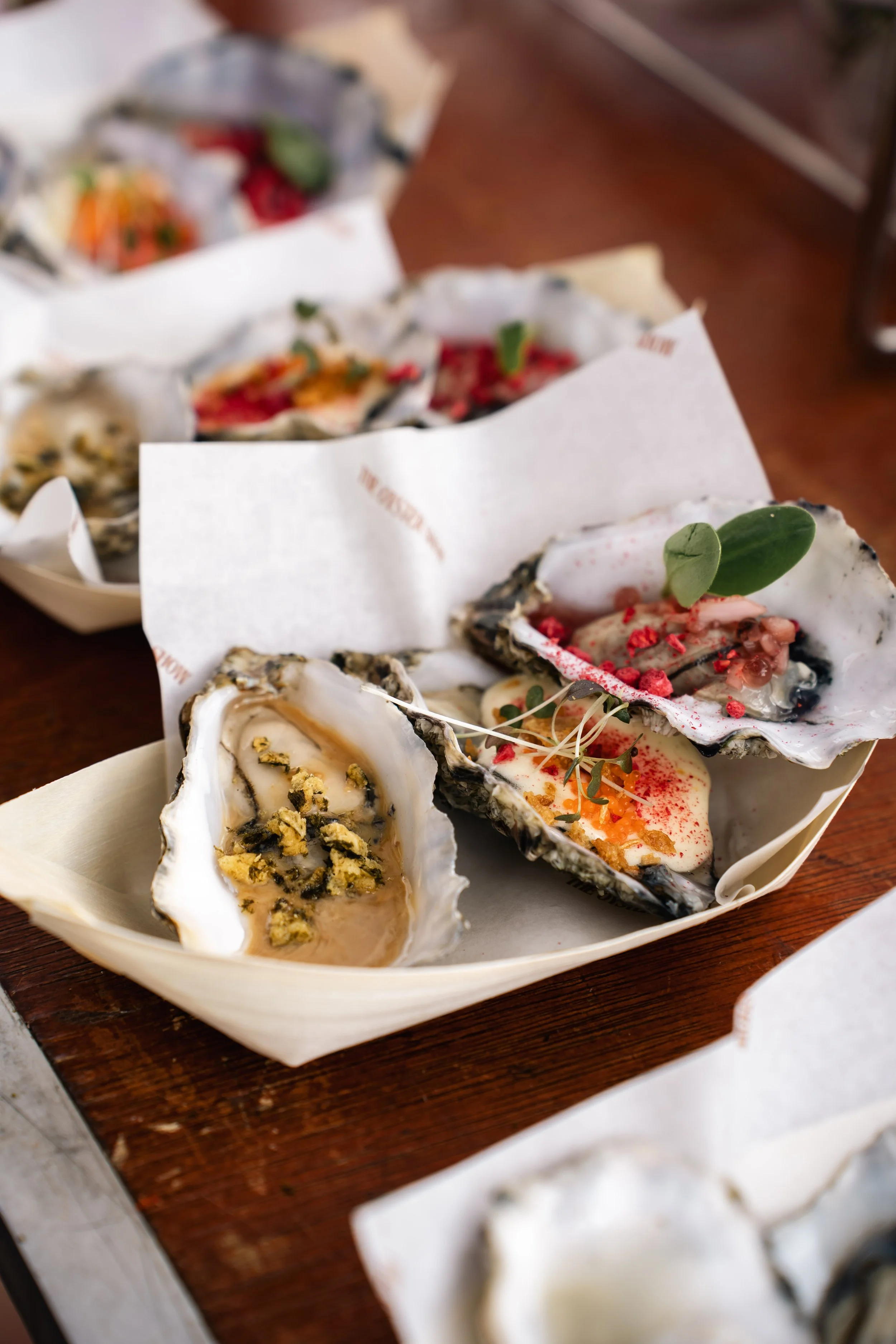 Verspreide oesters met verschillende toppings op een houten tafel.