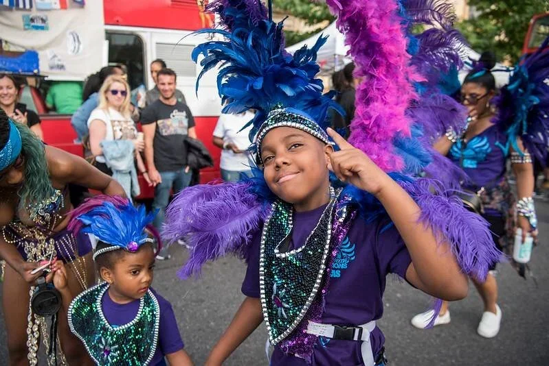 A person holding a microphone on their lap, they are wearing a colourful purple robe with embroidered sleeve.