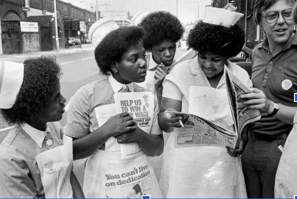 A group of black nurses gather to look at protest leaflets
