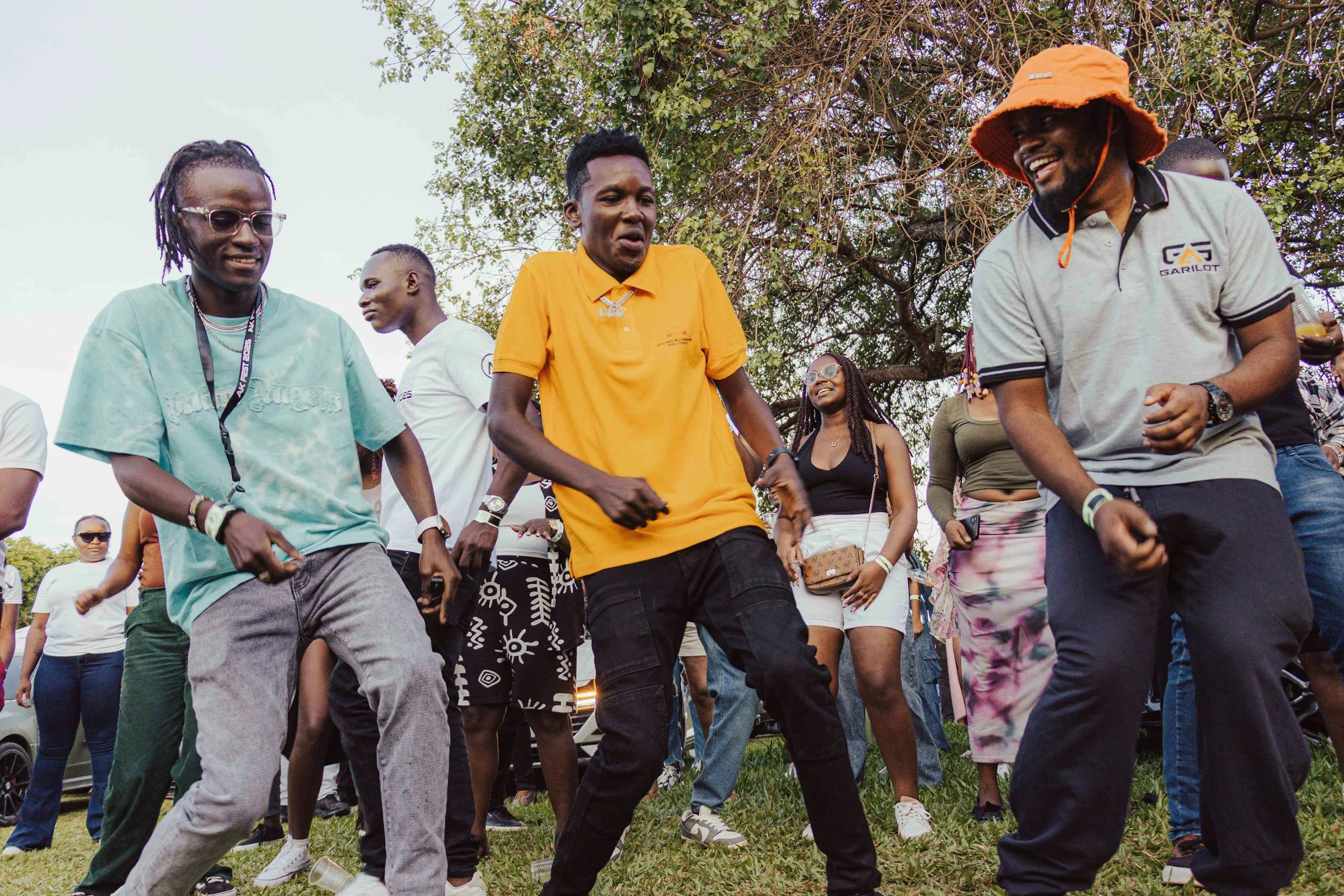 A group of people dance in an outdoor space, wearing summer clothes, having fun.