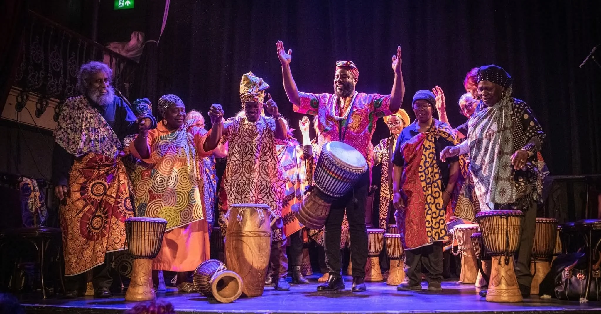 A group of people in African traditional dress play drums and raise their arms
